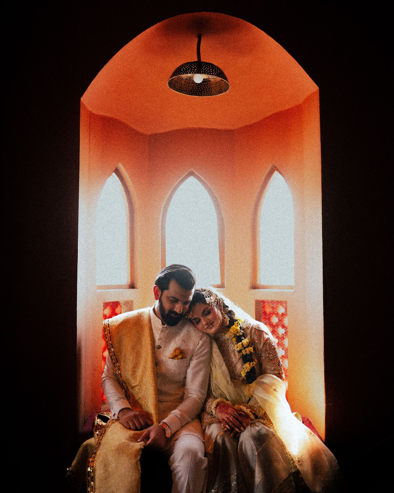 Romantic couple moment captured in orange-lit architectural alcove with arched windows.