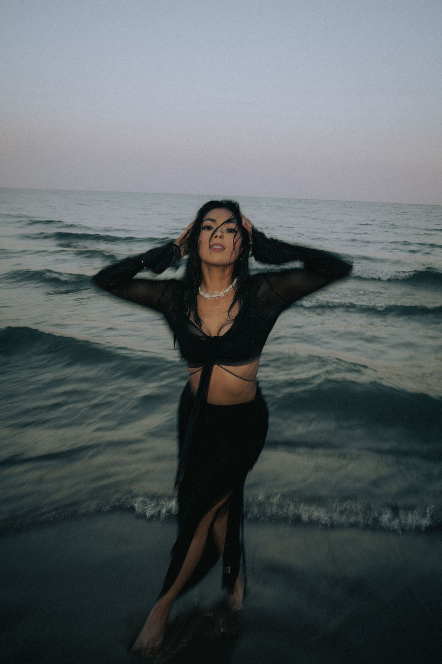 Dynamic beach photoshoot with flowing black dress against ocean waves.