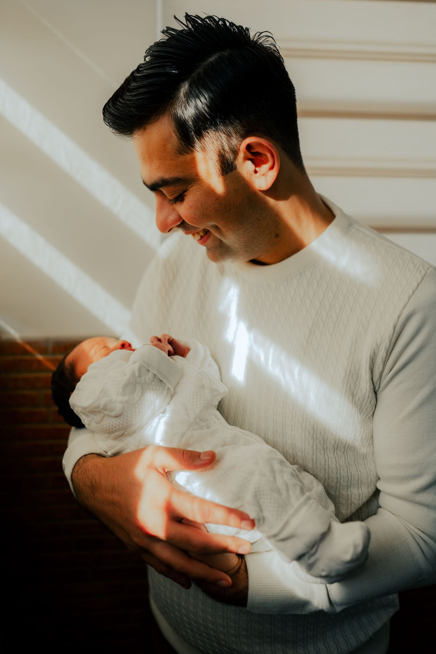 Tender moments of a parent holding their newborn baby in soft window light.