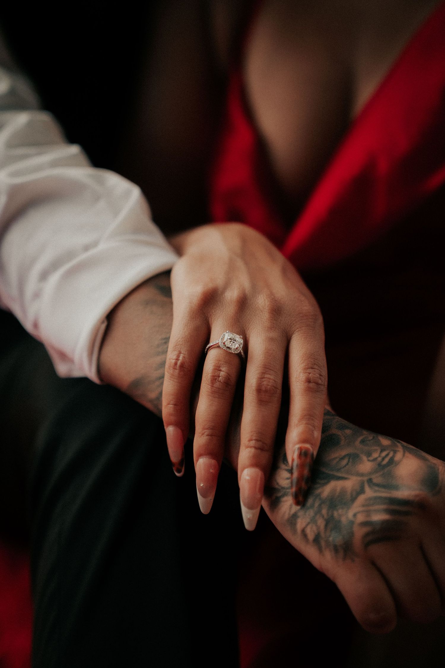 Close-up shot of hands showing off an engagement ring with visible tattoo artwork.