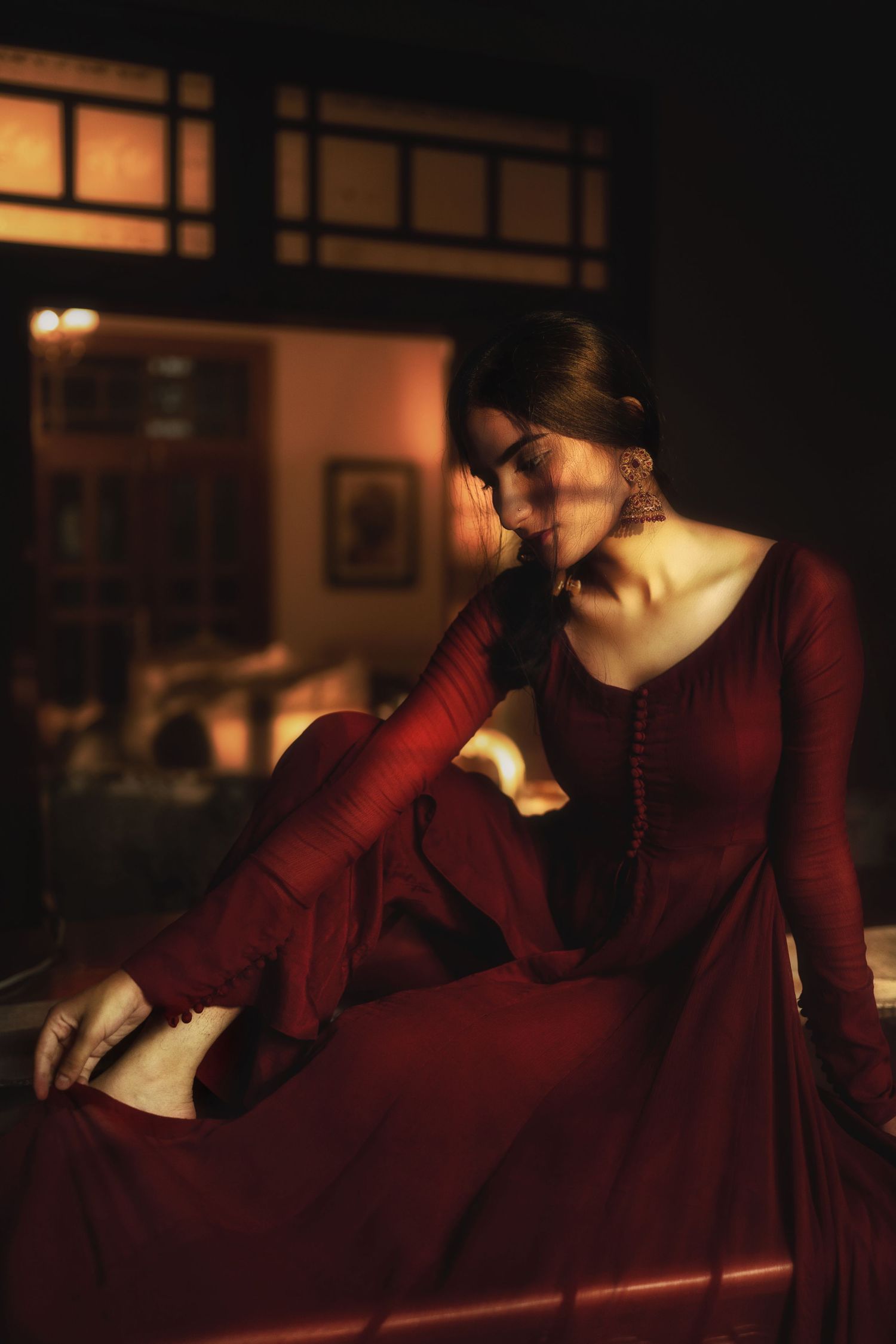 A moody indoor portrait featuring someone in a deep red vintage-style dress.