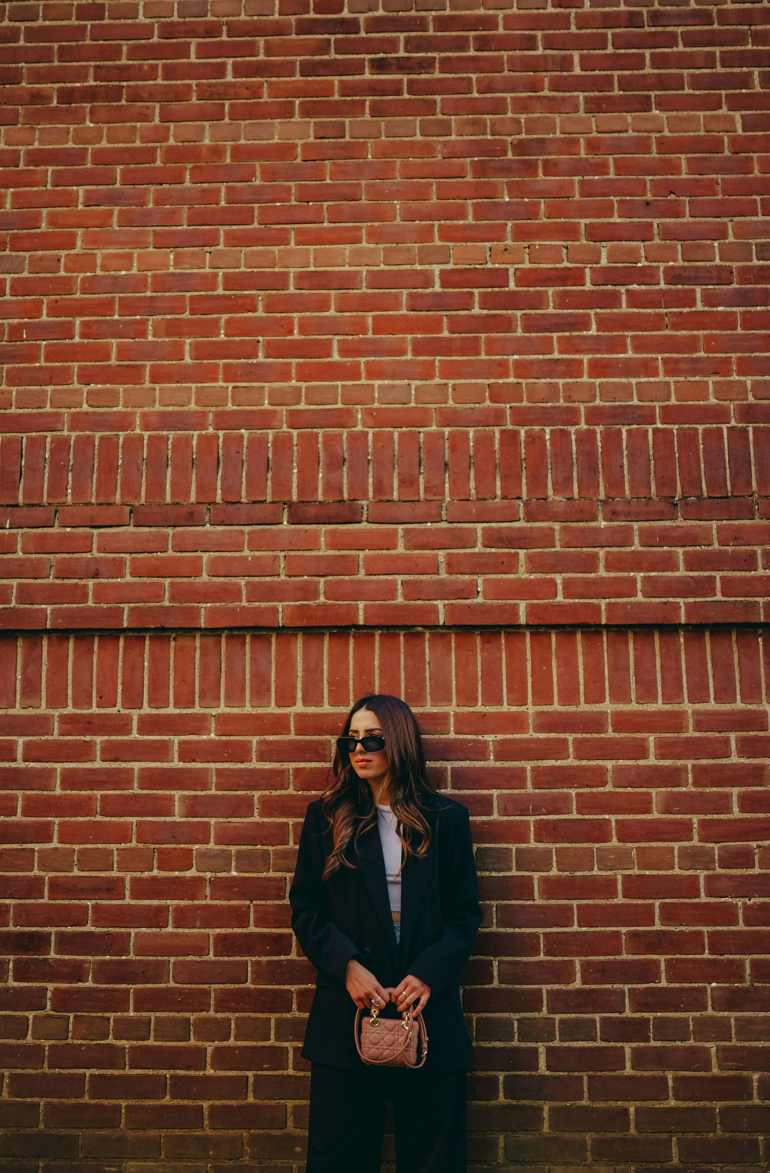 Fashion portrait against red brick wall wearing sunglasses and dark coat.
