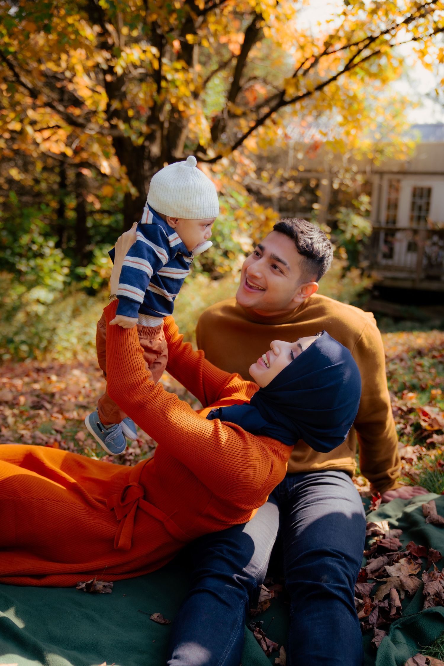 Couple playfully interacting while lying on autumn leaves in an outdoor setting.