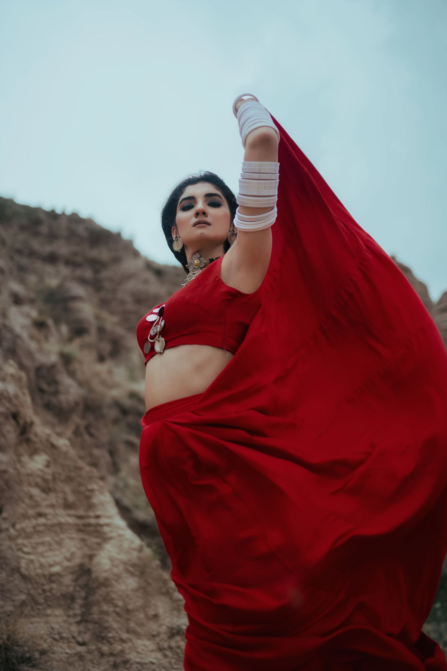 Flowing red fabric catches wind as figure poses dramatically against rocky backdrop.