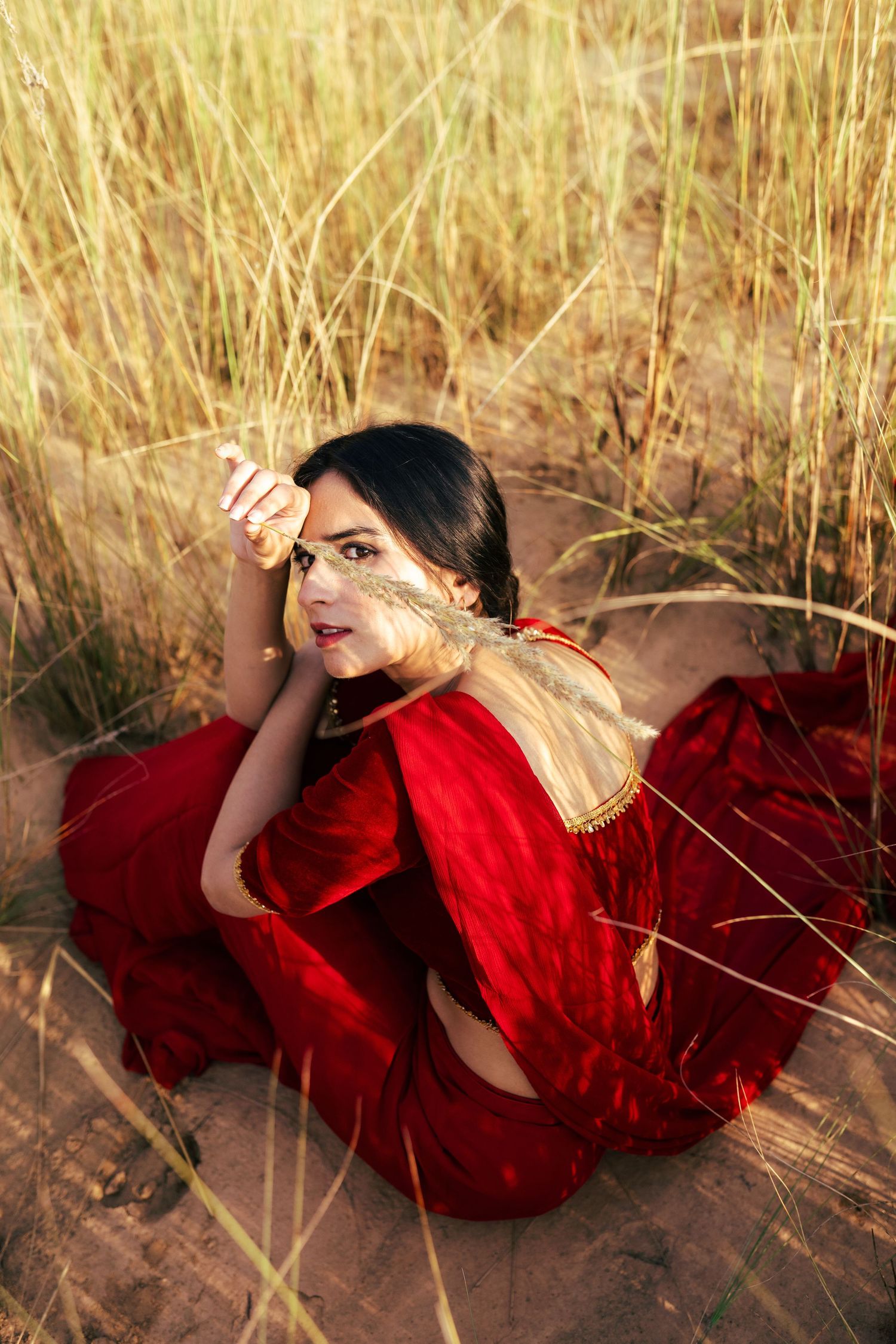Dramatic fashion photos of someone lying in tall golden grass wearing a flowing red dress.