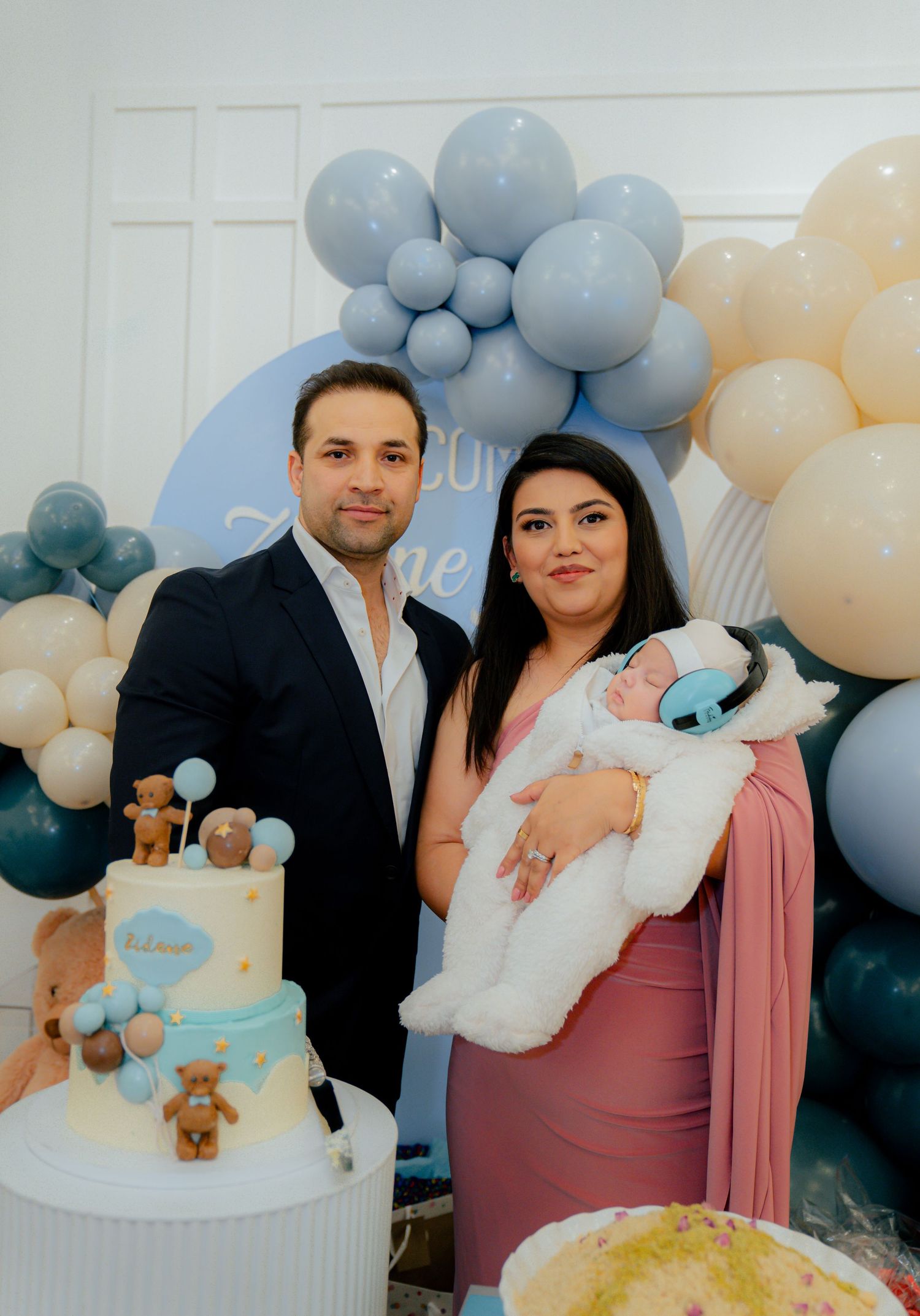 A baby celebration with blue and cream balloon arch, teddy bear cake, and elegant party decor.