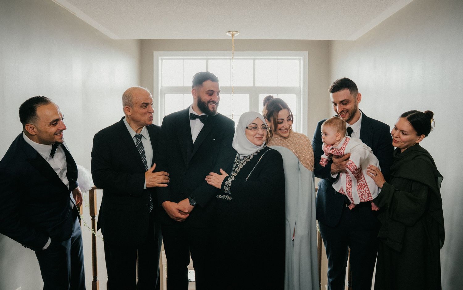 Wedding party in formal attire sharing laughs in bright indoor setting.