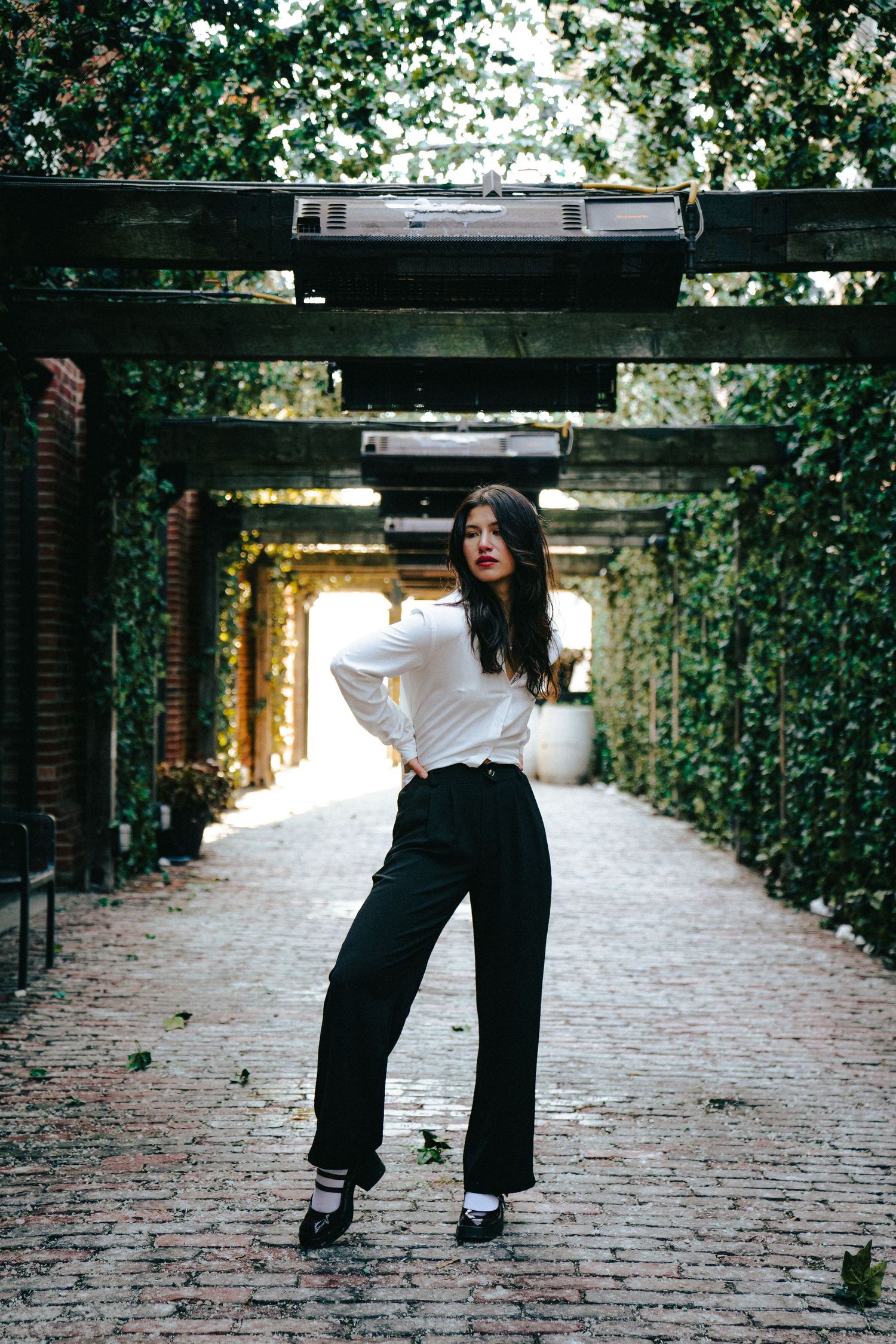 Artistic fashion shots of wide-leg pants on cobblestone path under wooden pergola.