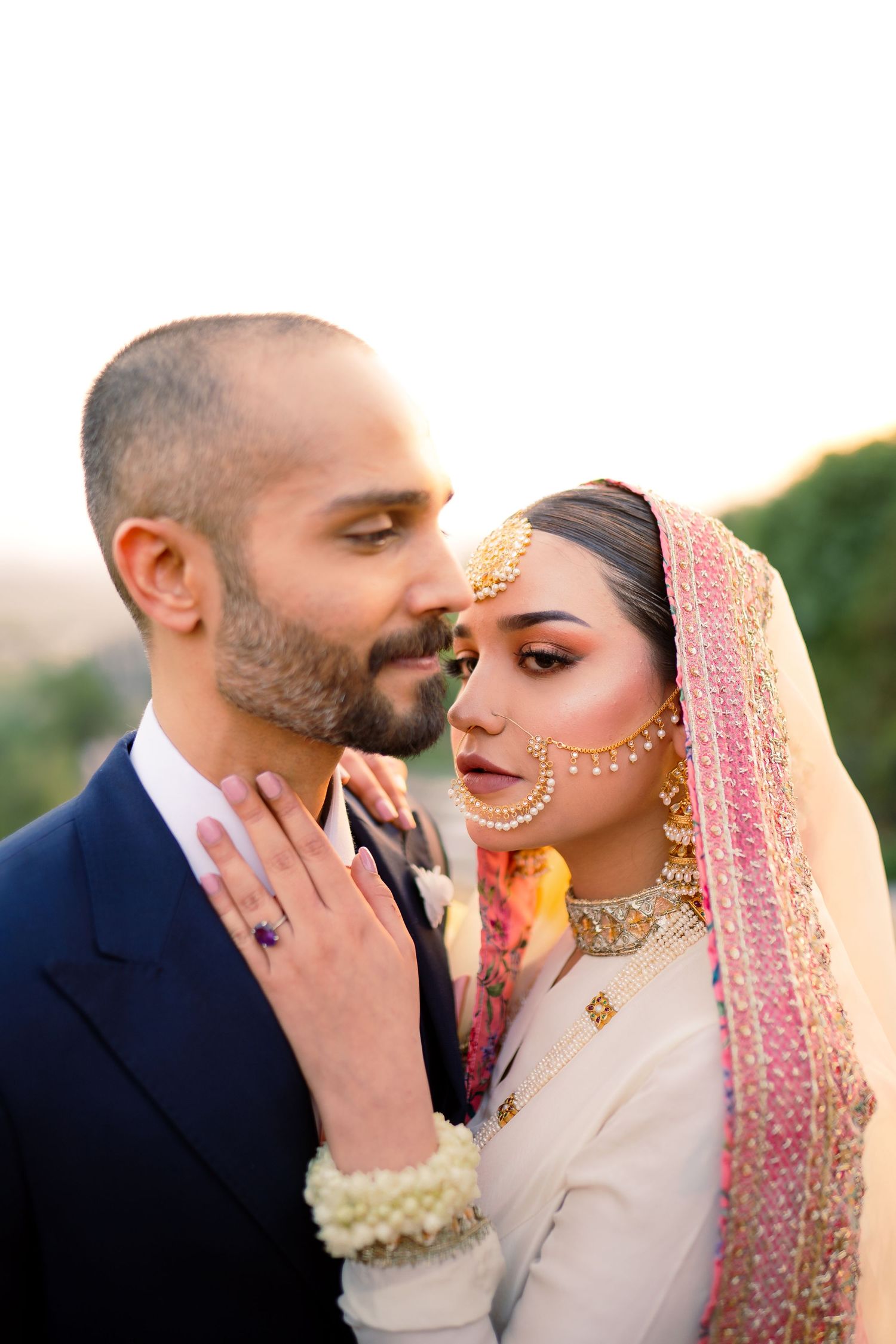A tender moment between a couple in traditional South Asian wedding attire during golden hour.
