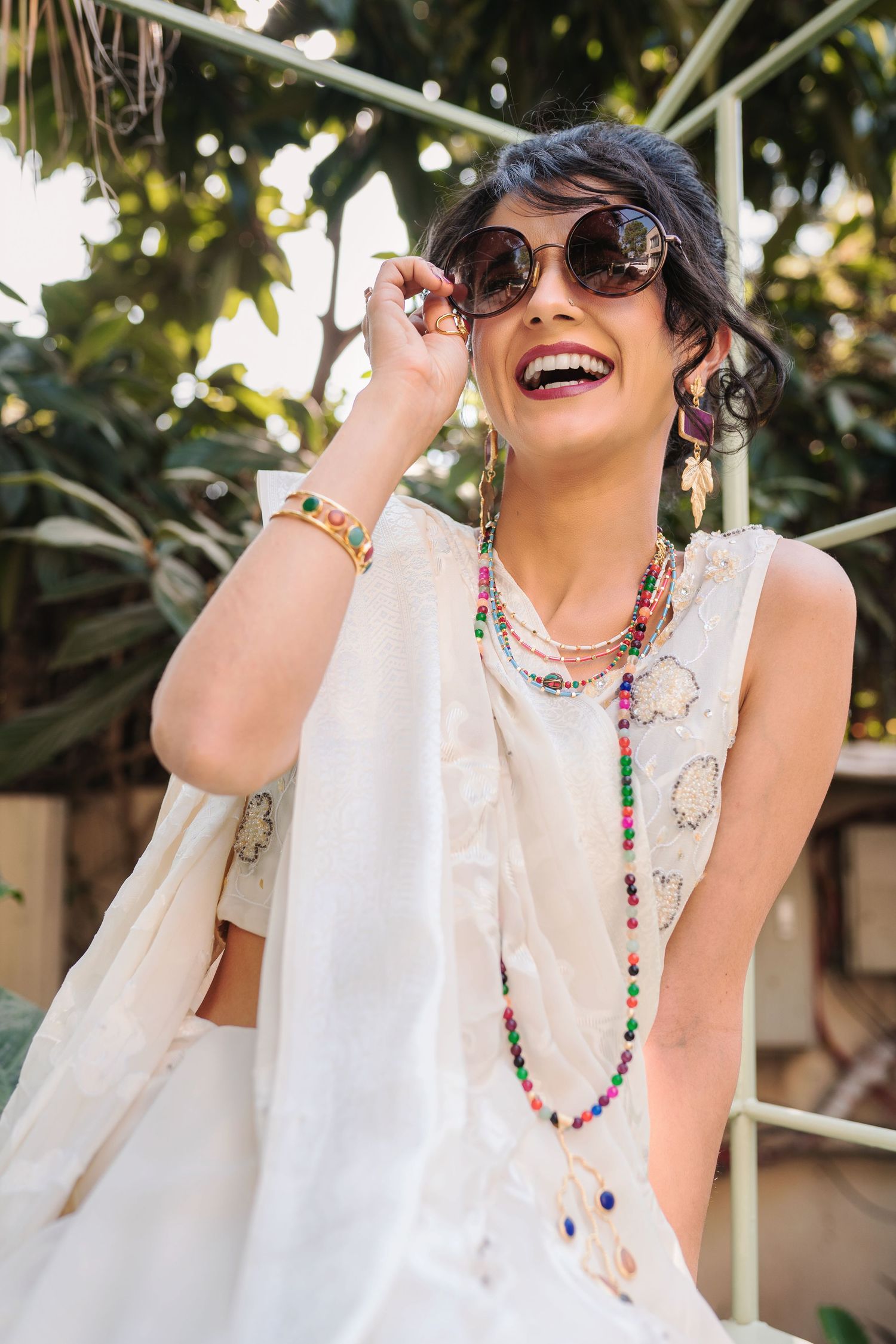 Person in white sleeveless top and colorful necklace laughing joyfully in outdoor setting.