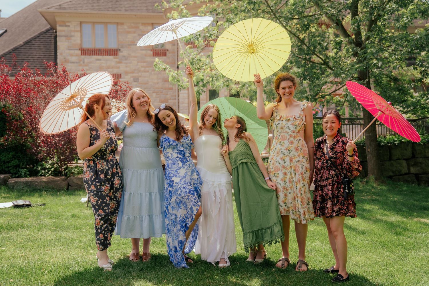 Group photo at garden party with colorful parasols and vintage-style summer dresses.