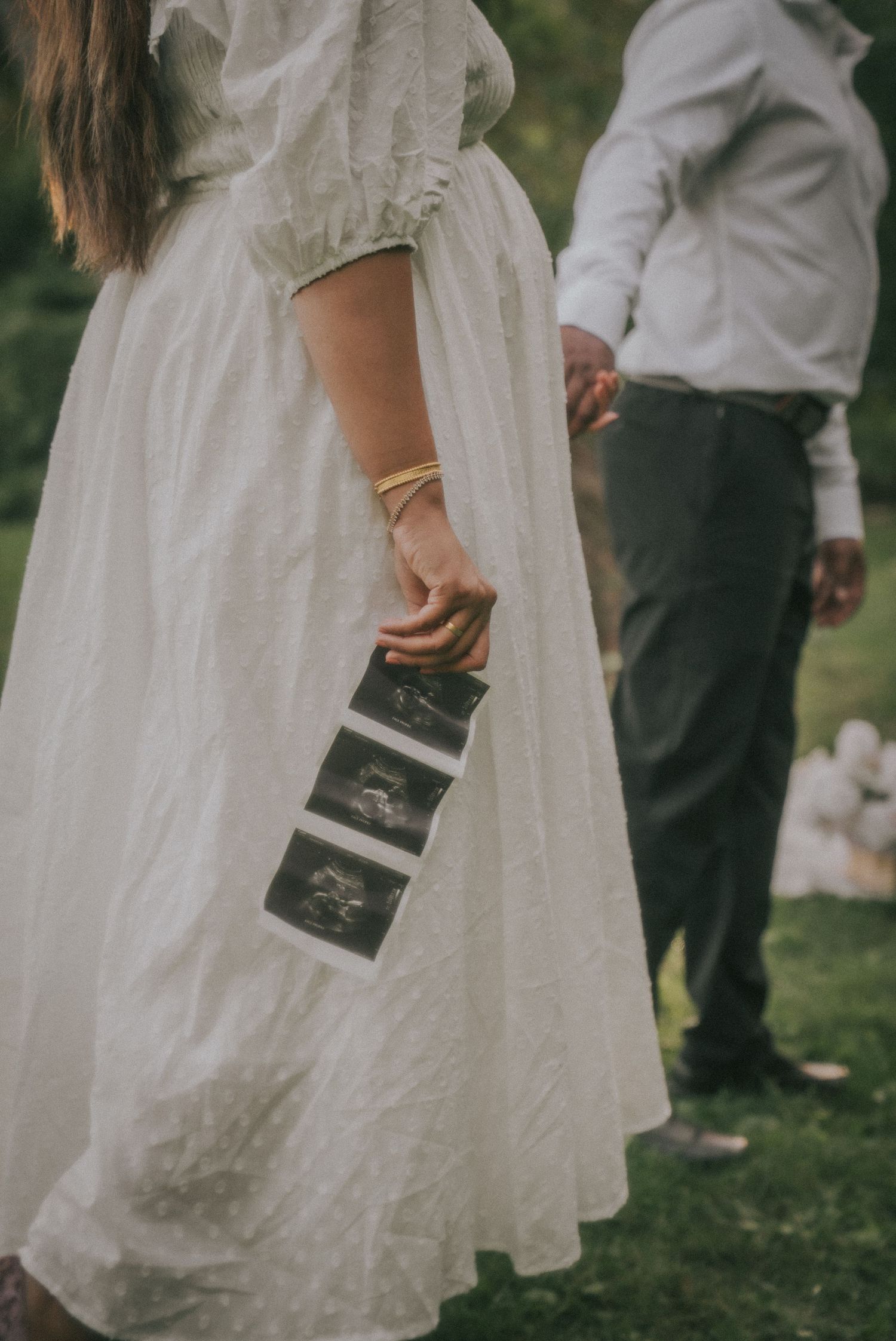 Close-up of white dress details and hands holding a small book outdoors.