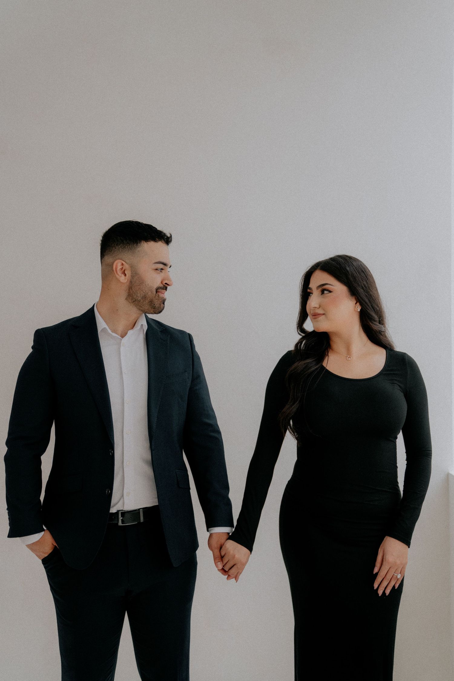 A stylish couple in matching black outfits poses against a minimalist grey background.