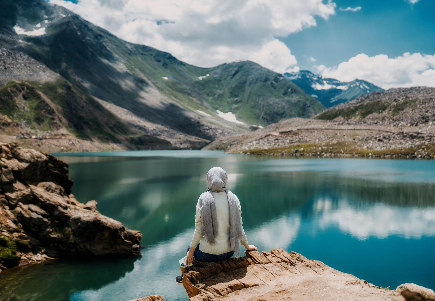 Panoramic mountain landscape with turquoise alpine lake surrounded by rocky terrain.