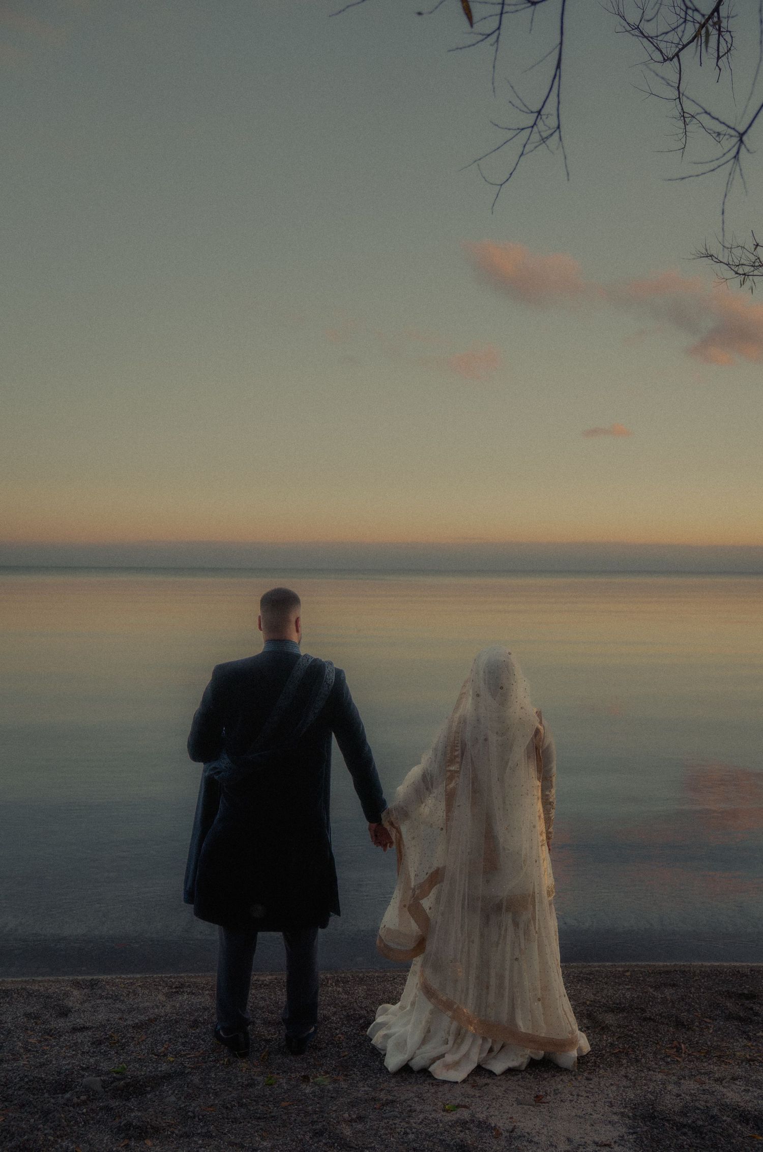 Wedding couple stands silhouetted against sunset sky on scenic overlook.