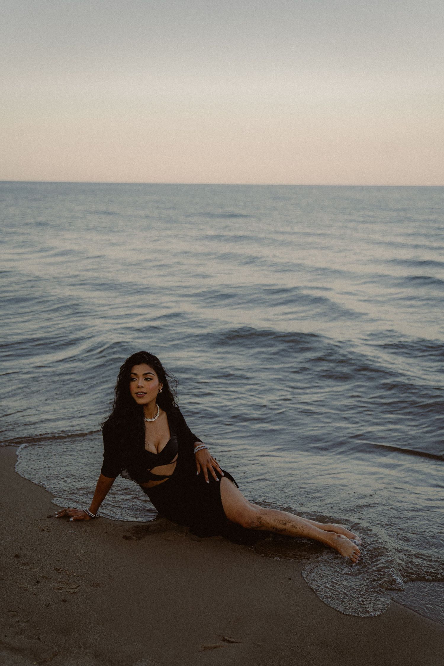 Artistic beach photoshoot with waves and sand featuring black attire at sunset.