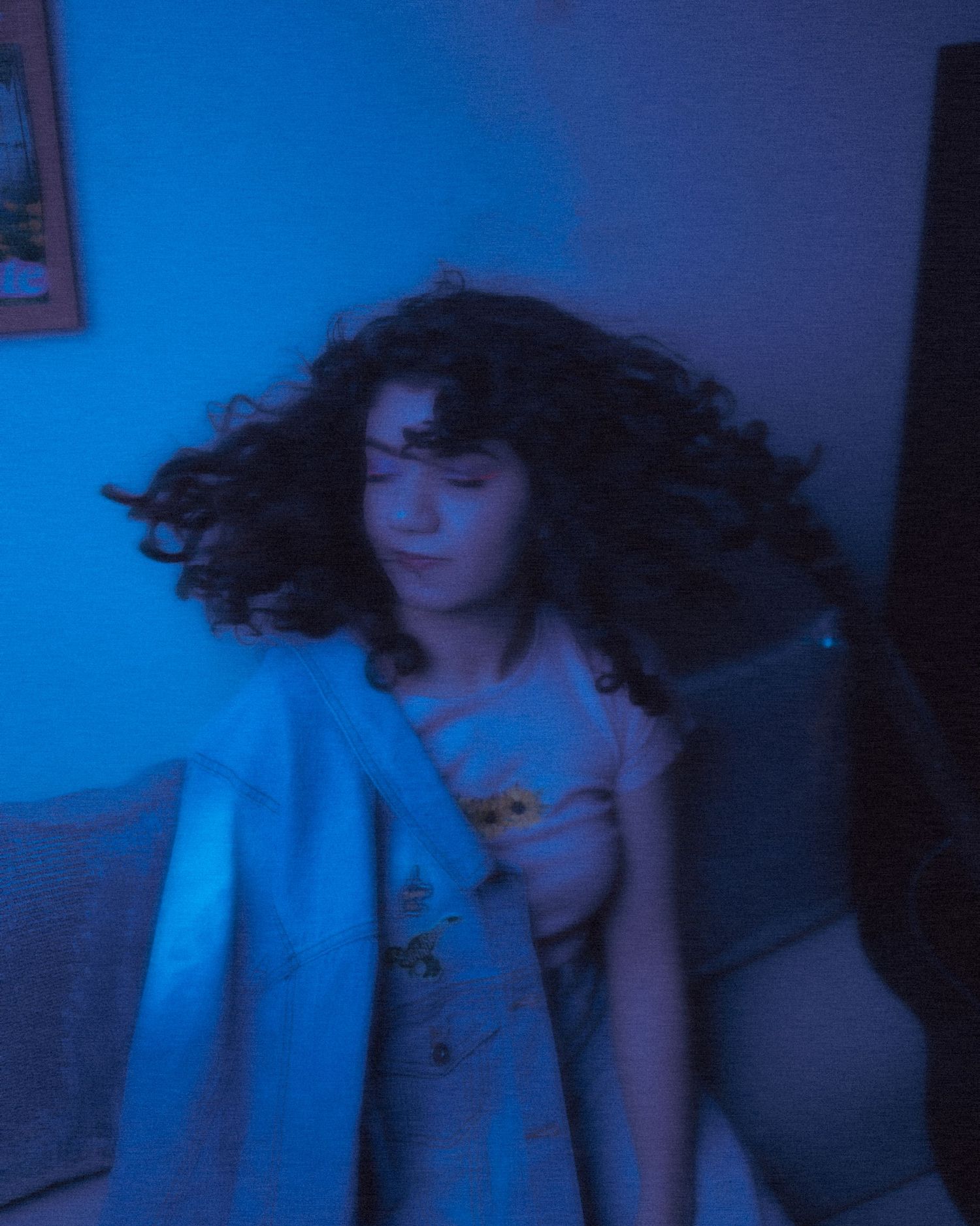 Artistic blue-tinted portrait of someone with curly hair in motion against a dark background.