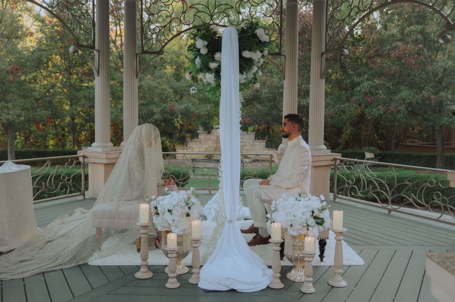 Outdoor wedding ceremony setup with white columns and garden backdrop.