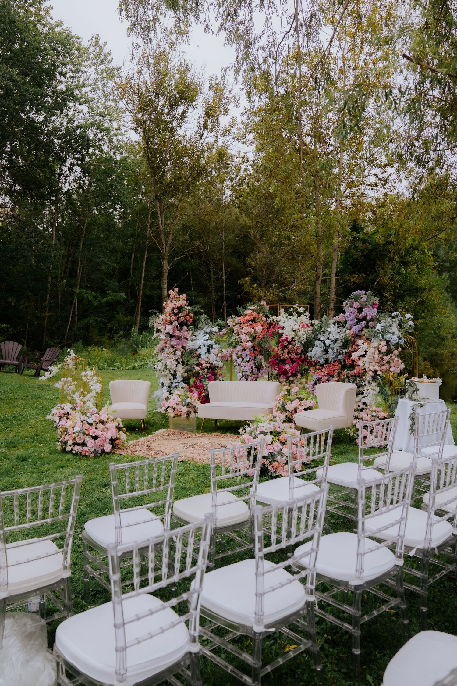 Clear acrylic chairs decorated with floral arrangements set up for an outdoor ceremony.
