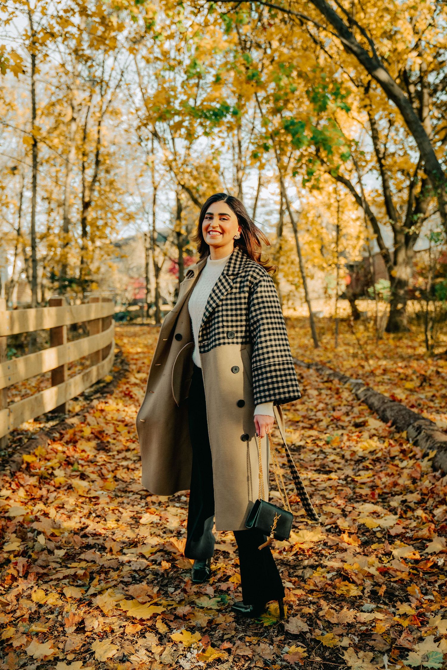 Autumn fashion shoot with long coat and handbag among fallen yellow leaves.