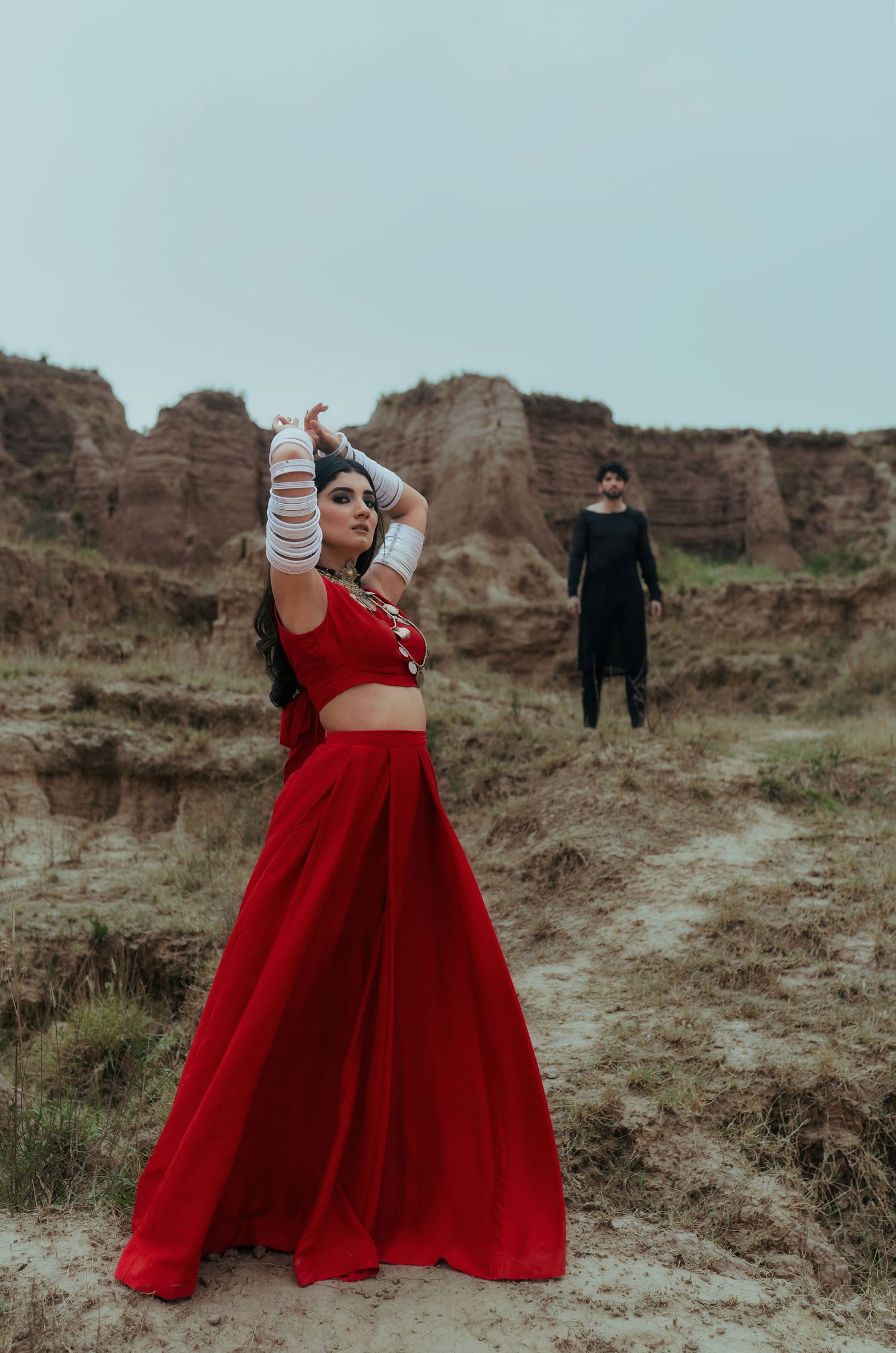 A dramatic pose in a flowing red dress against rocky cliffs and desert landscape.