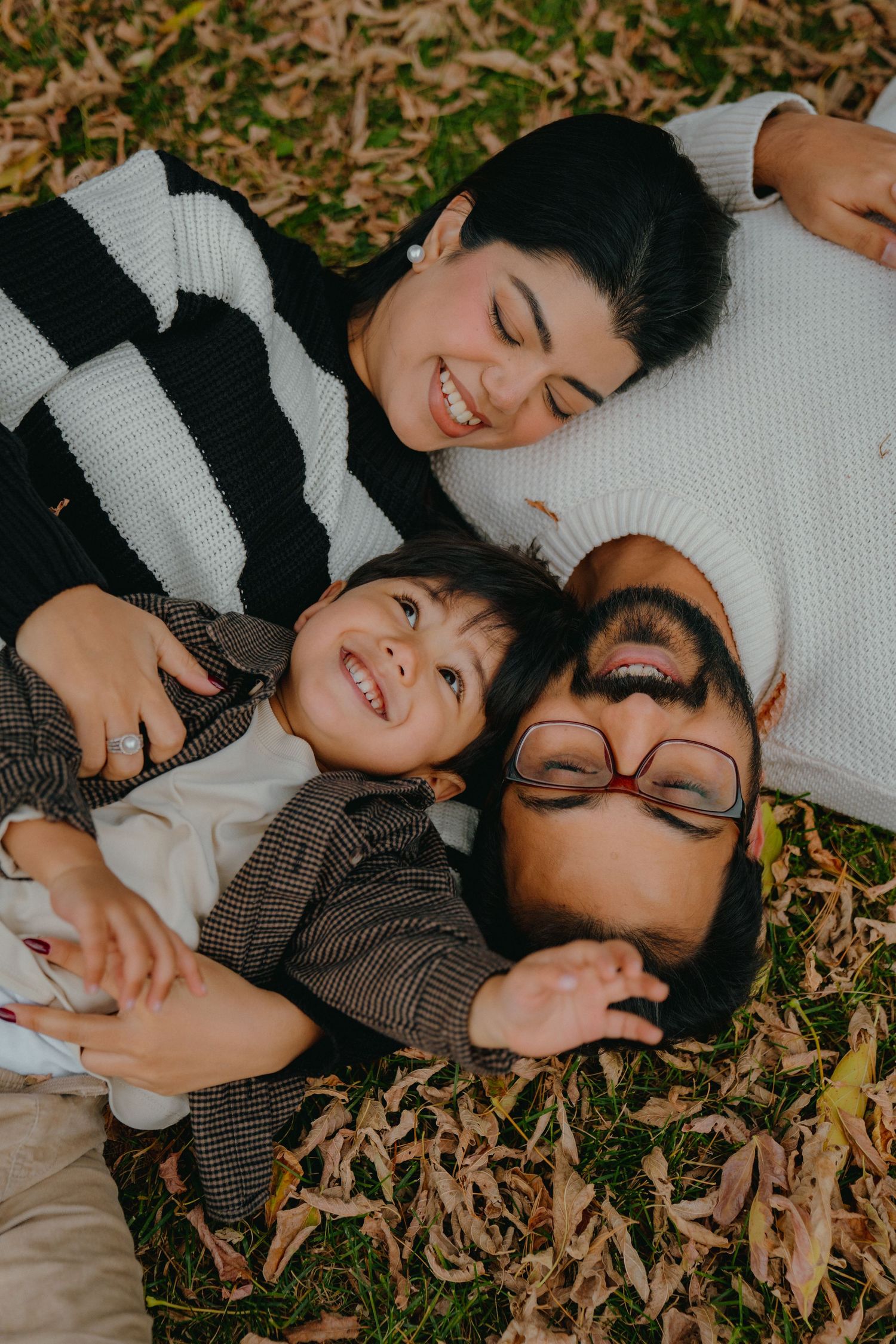 Friends lying on autumn leaves in cozy sweaters sharing a joyful moment.