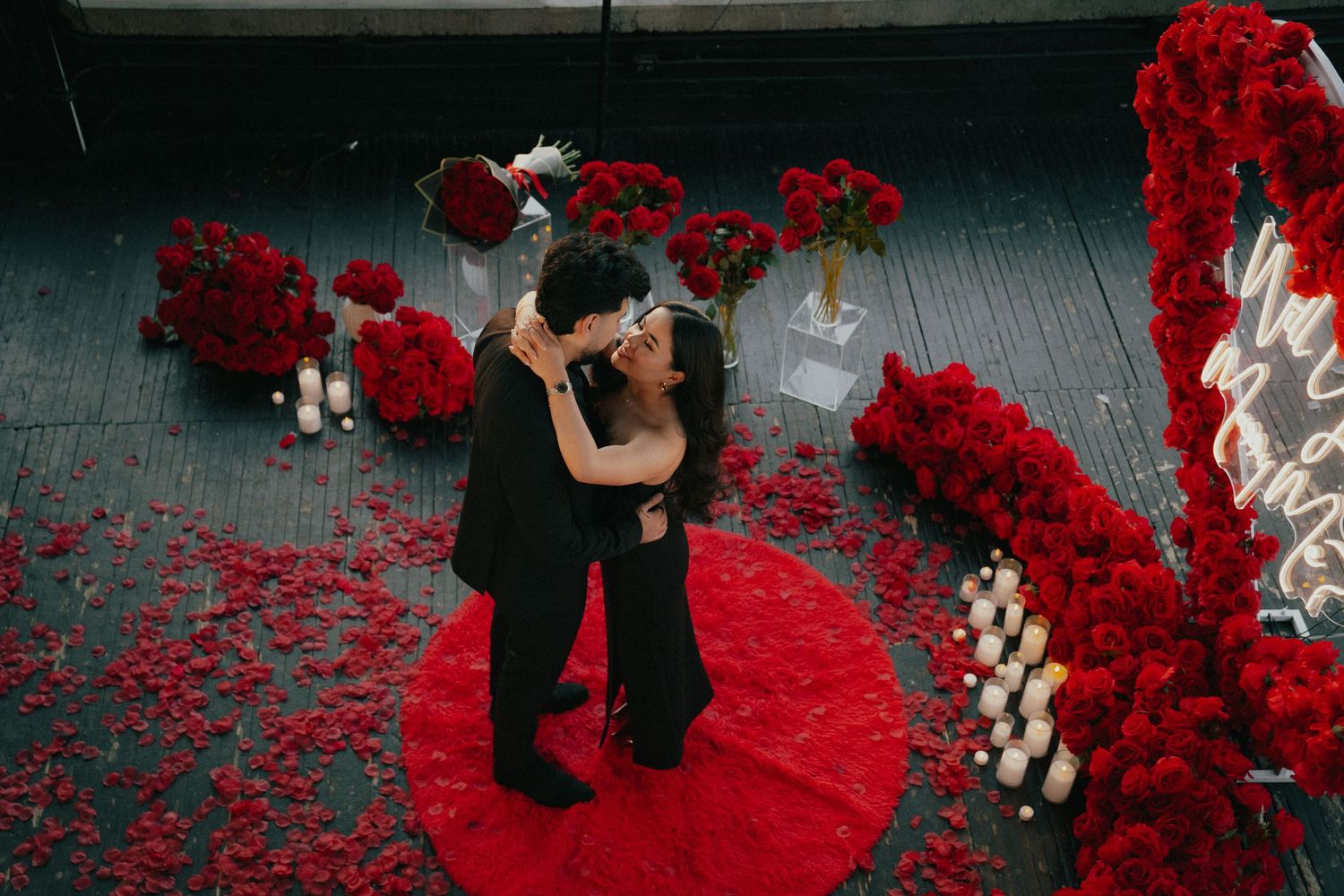 Romantic scene with couple on red rose petals surrounded by white candles.