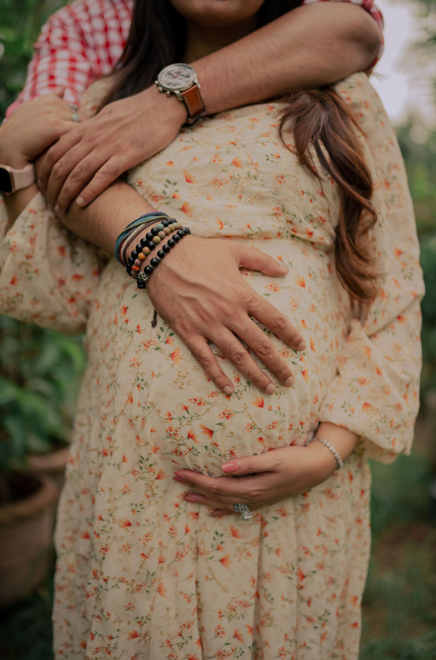 A series of hands lovingly touching a floral print maternity dress showing a growing baby bump.