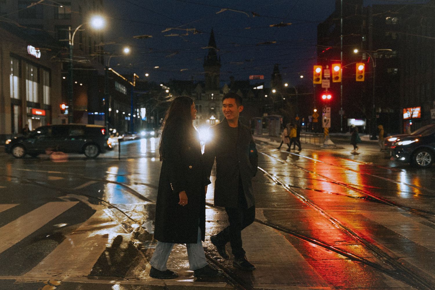 Rainy city street at night with reflective wet pavement and traffic lights.