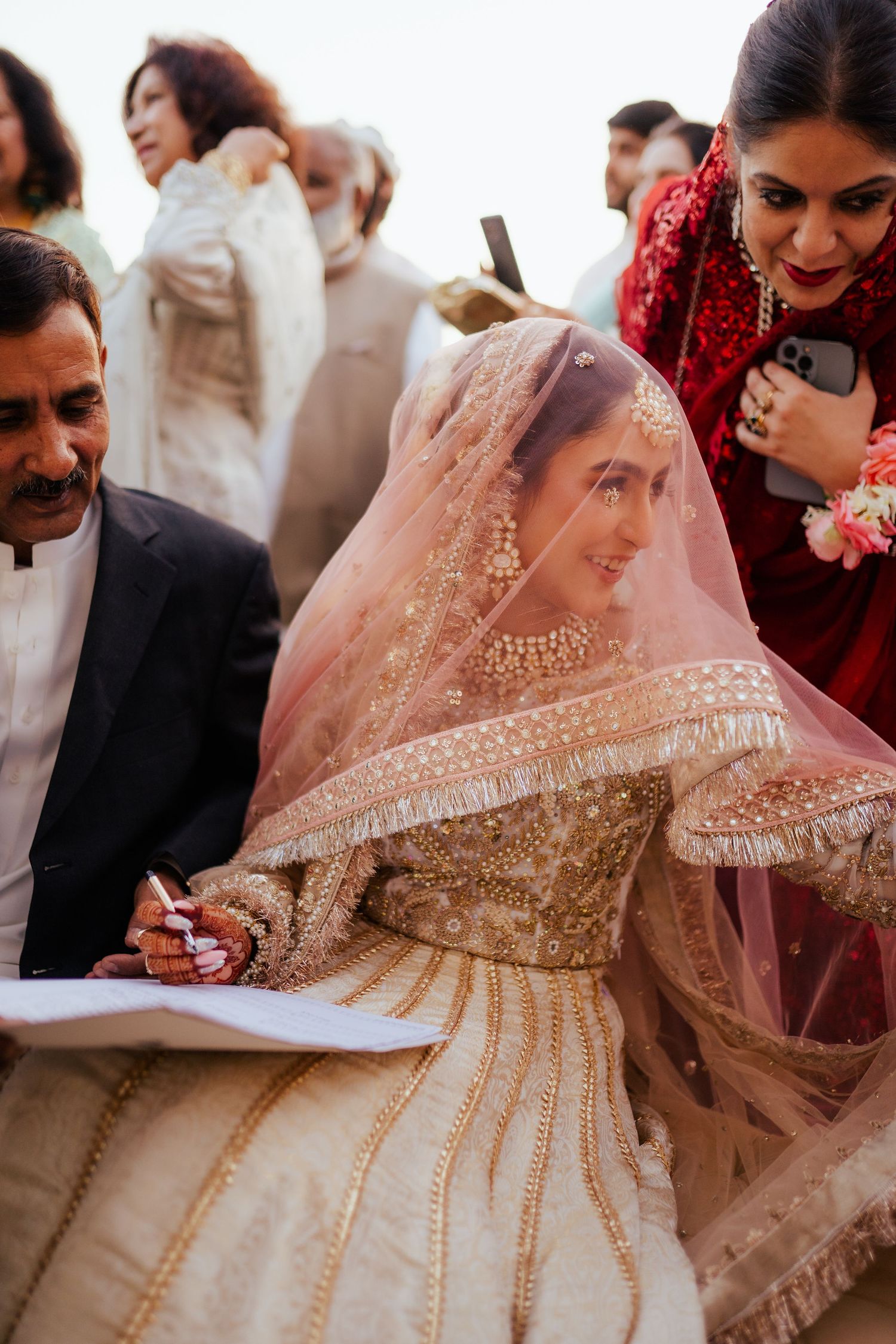 Wedding ceremony showing signing of marriage documents with ornate bridal dress details.