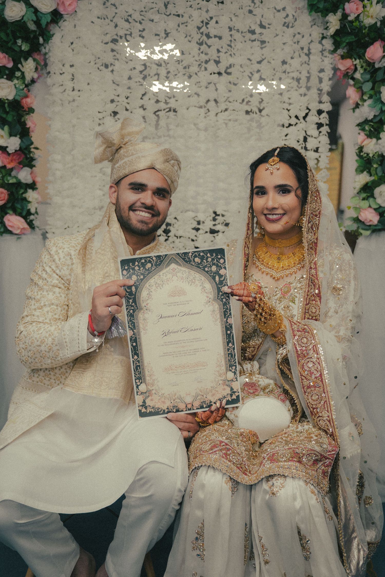 Newlywed couple in traditional South Asian attire holding their marriage certificate.