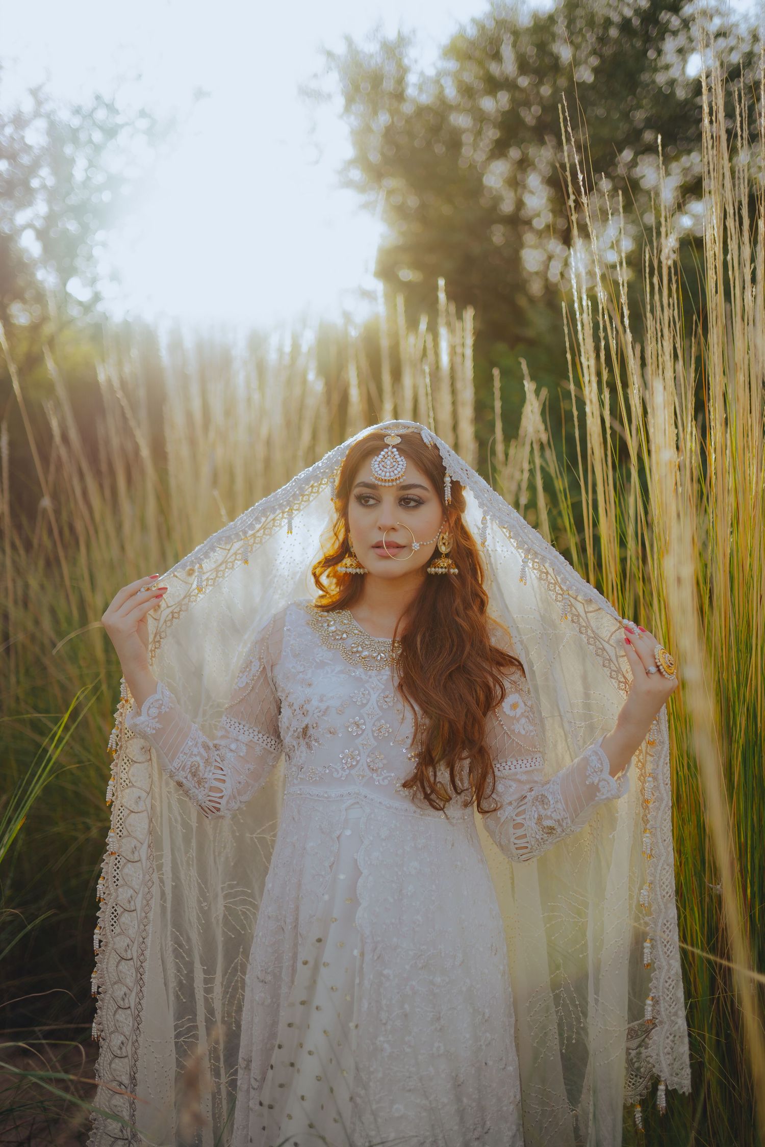 Dreamy bridal portraits in white lace dress among tall wheat fields at golden hour.