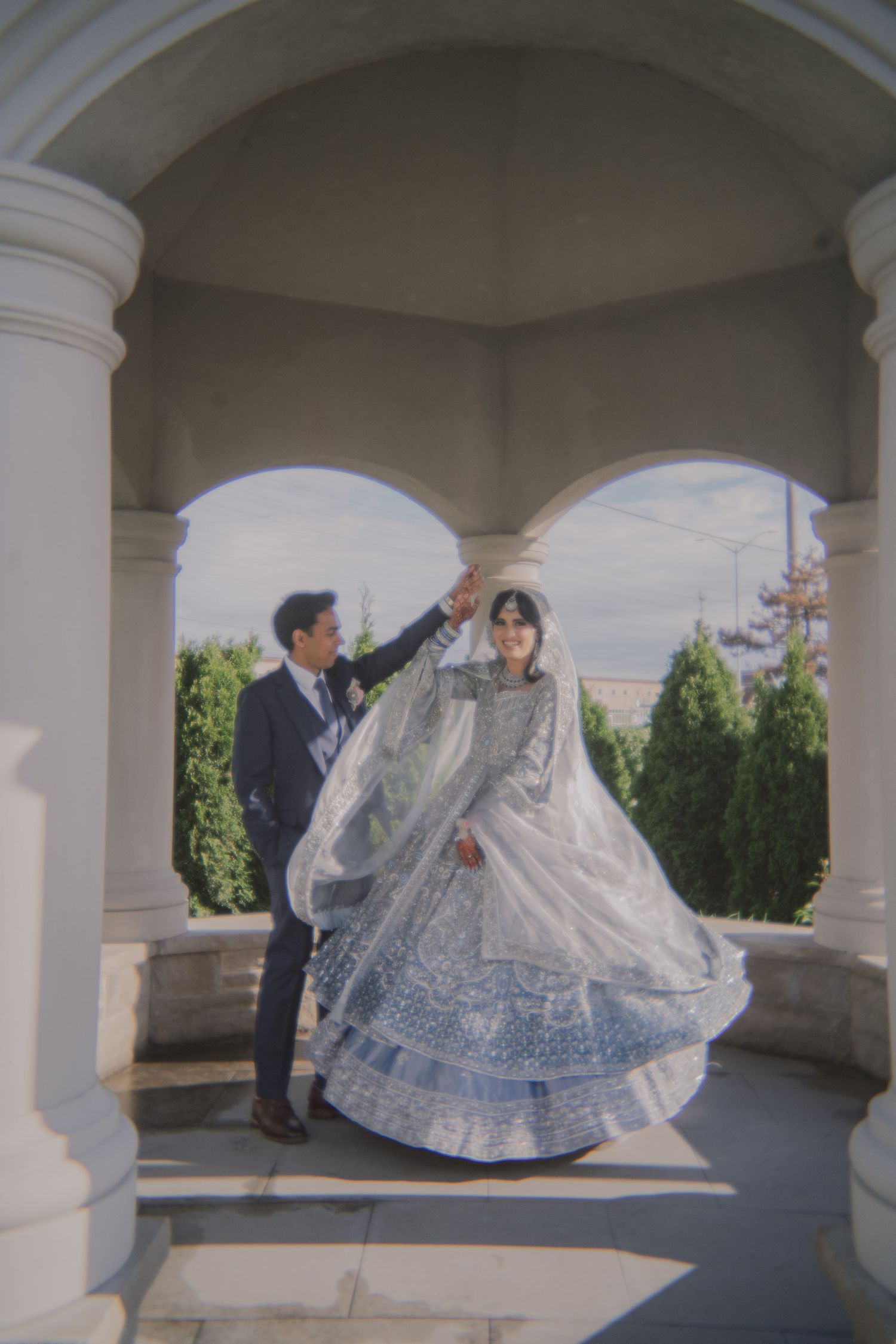 Ornate wedding dress with blue details twirls under white columned archway.
