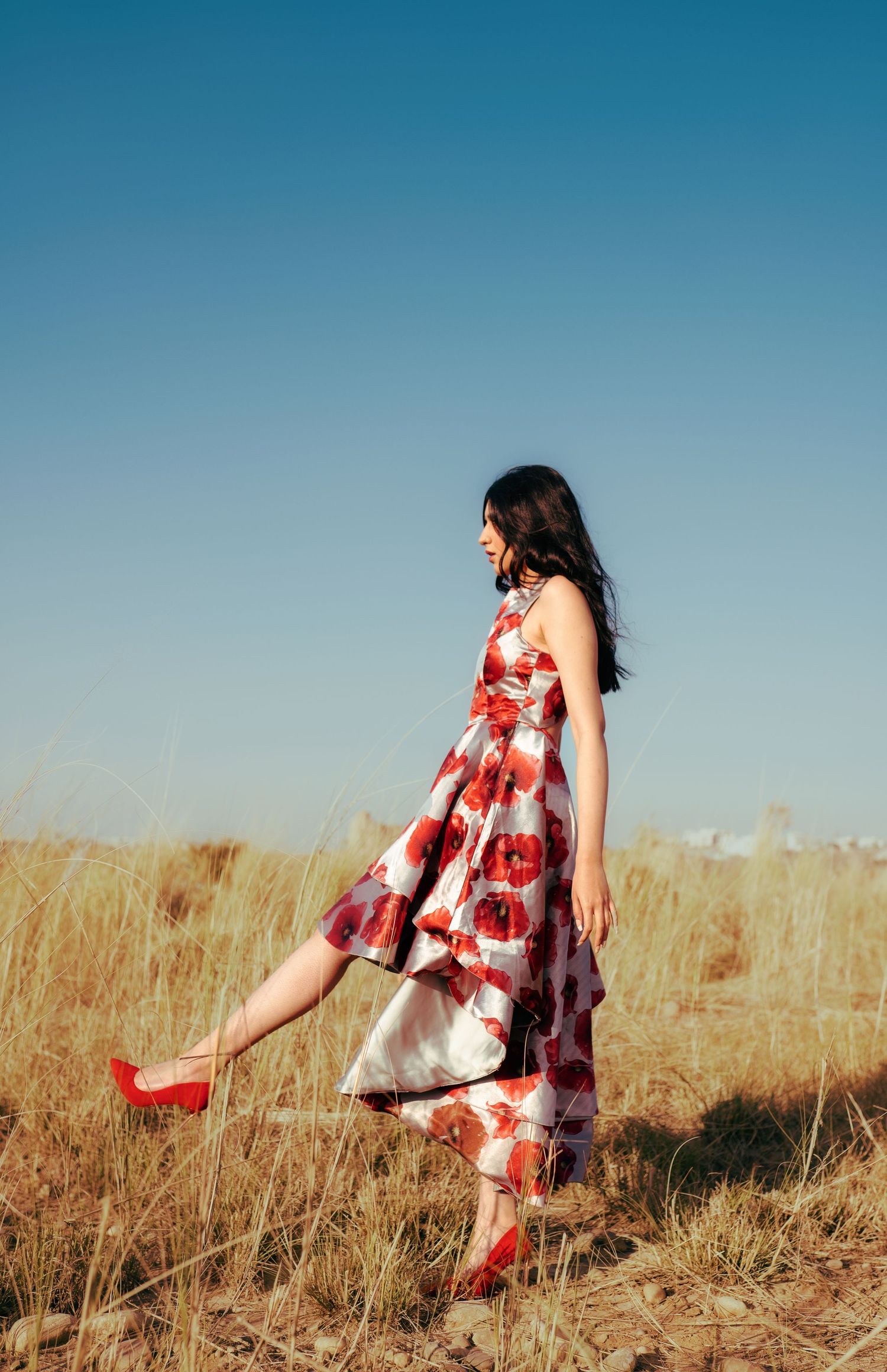 Dancing through tall grass in red and white floral dress.