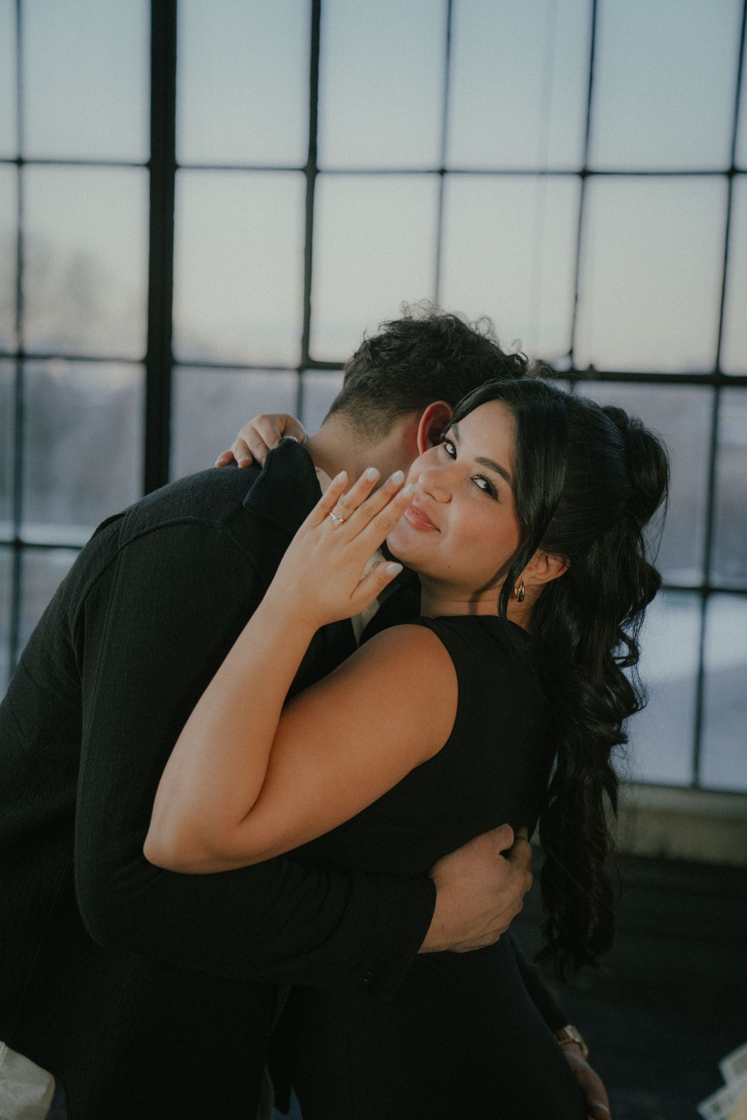 Intimate couple portrait in dark moody lighting against industrial windows.