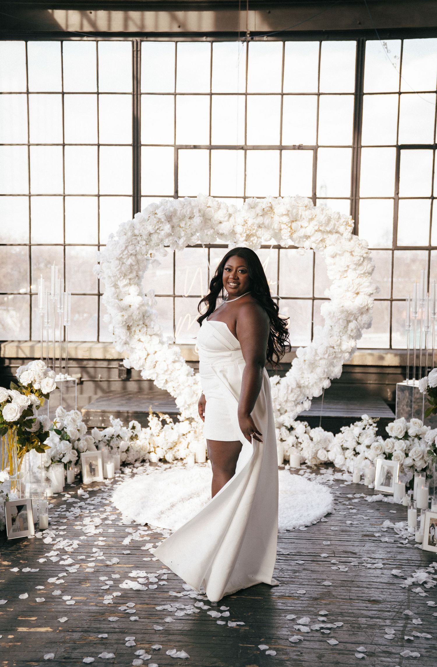 A white wedding dress twirls gracefully in an industrial space filled with white floral arrangements.