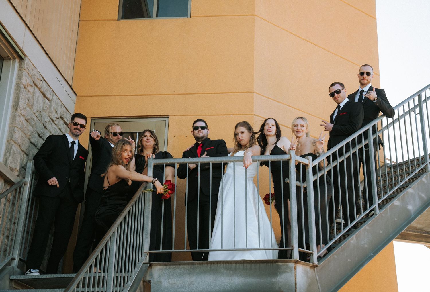 Wedding party poses along modern building balcony in formal attire.