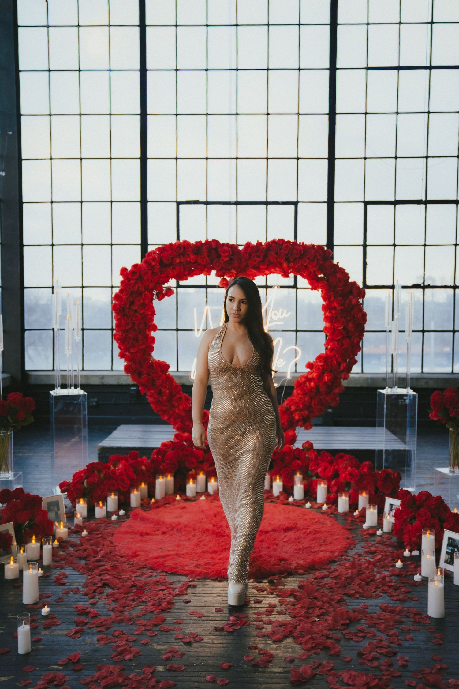 Romantic setup with heart-shaped red rose arrangements and white candles along glass windows.