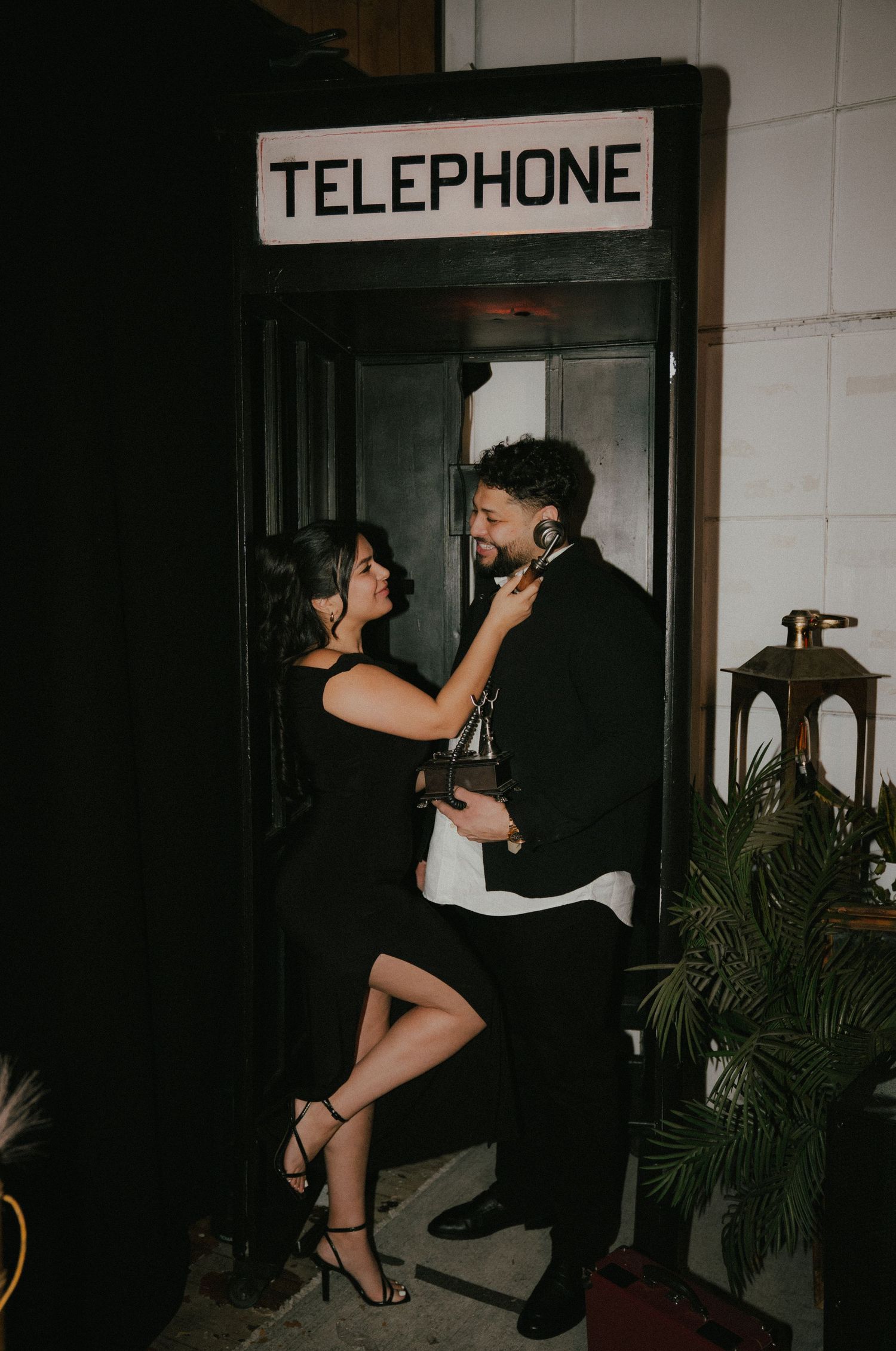 Stylish couple posing near vintage telephone booth in moody lighting.