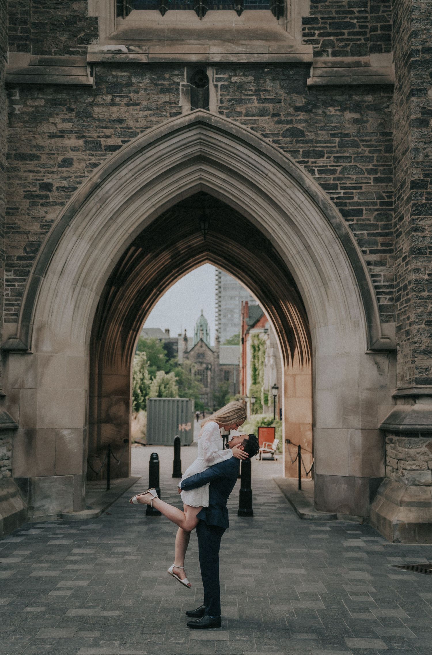 A couple performs a romantic dance pose under a Gothic stone archway at a historic building.