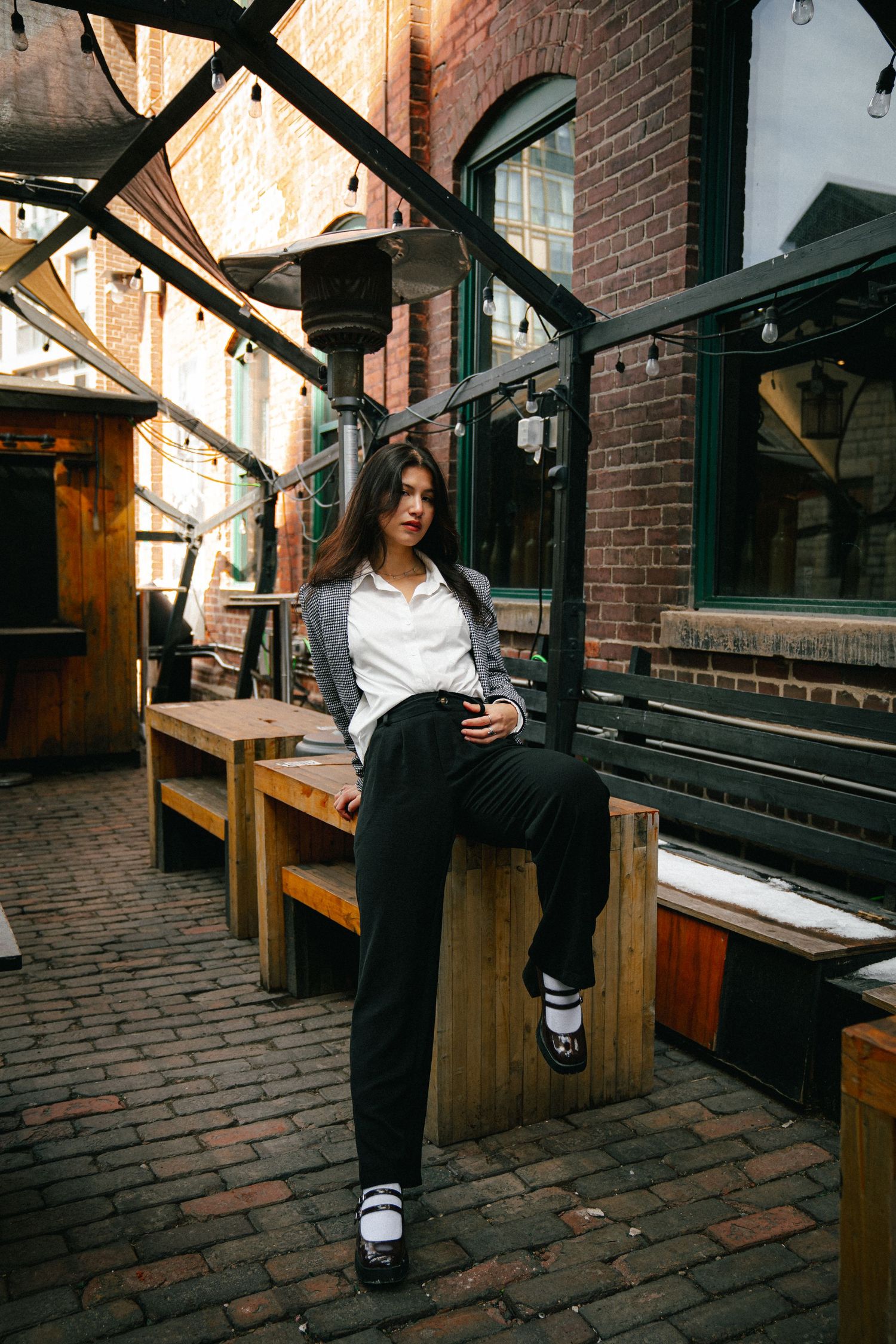 Person in casual attire sitting on wooden bench against brick wall background.