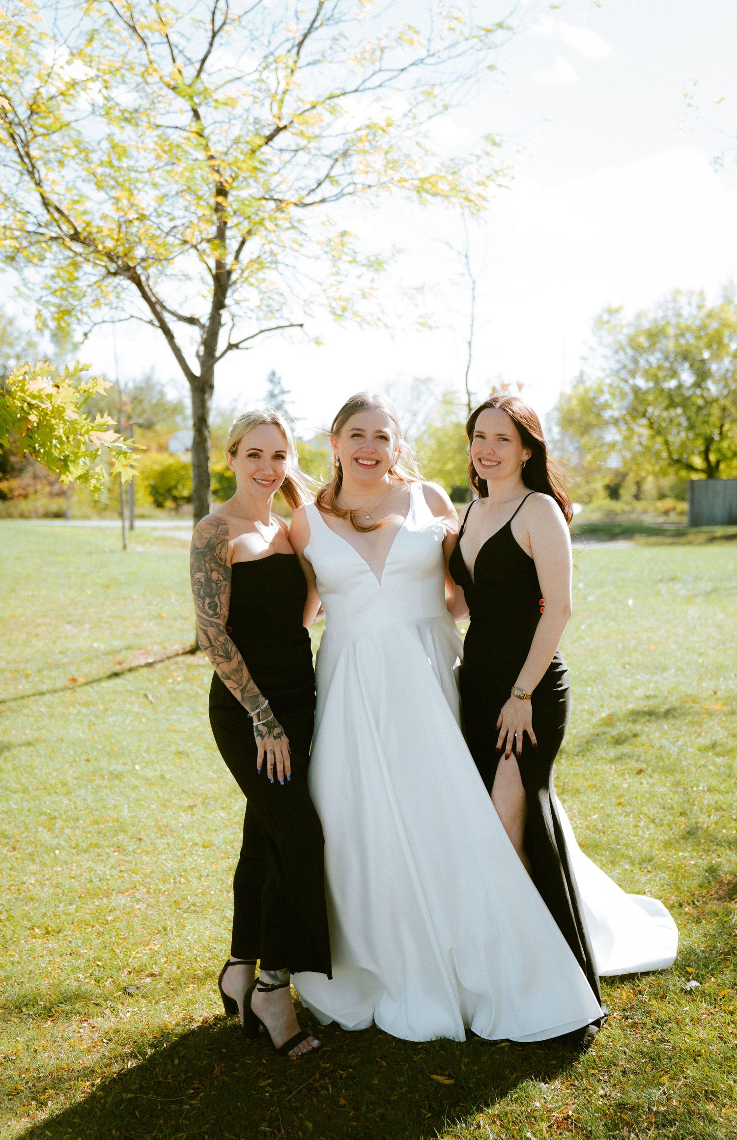 Wedding party poses on sunny grassy hill with autumn trees.