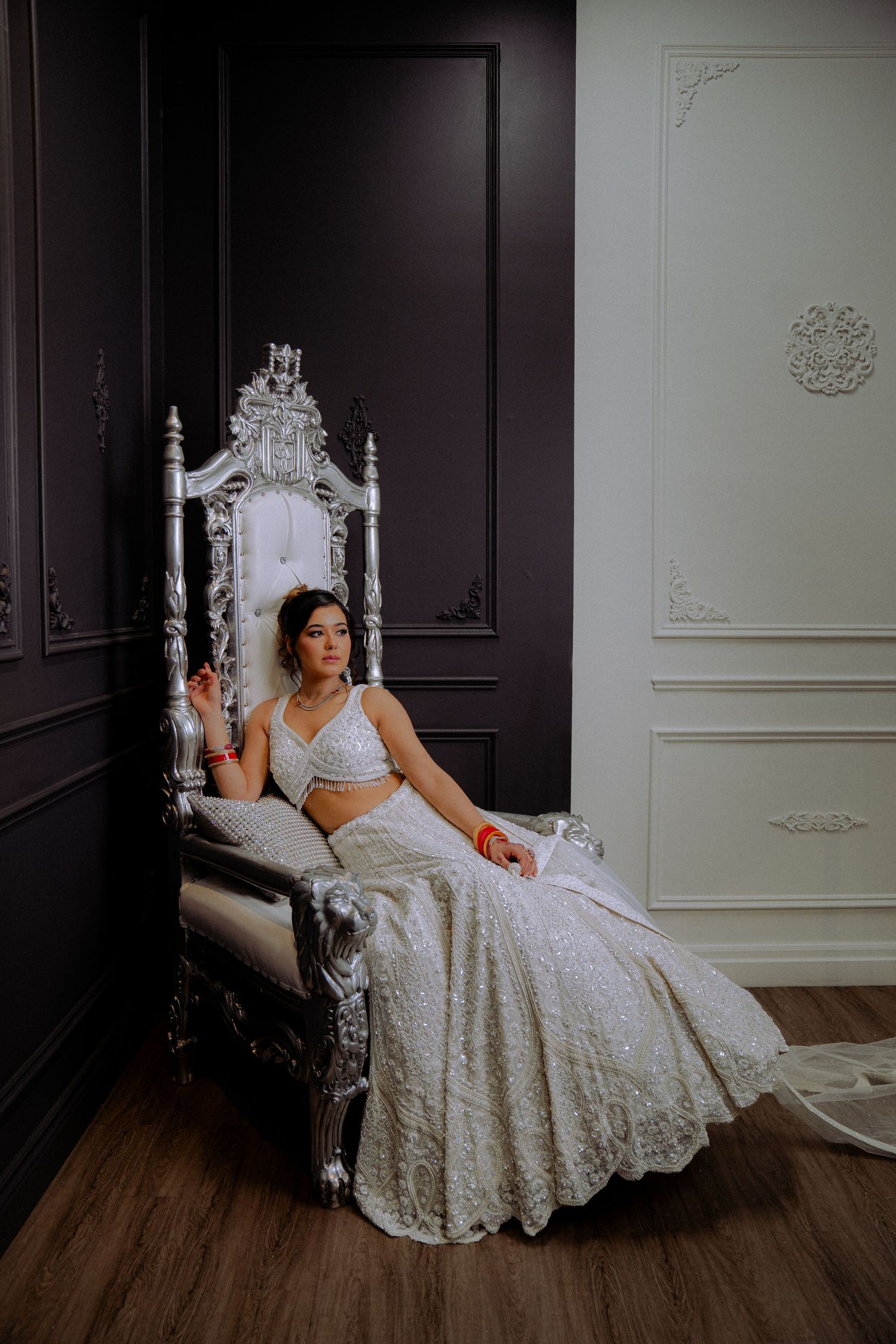 Elegant boudoir photography on ornate white bed against dark dramatic walls.