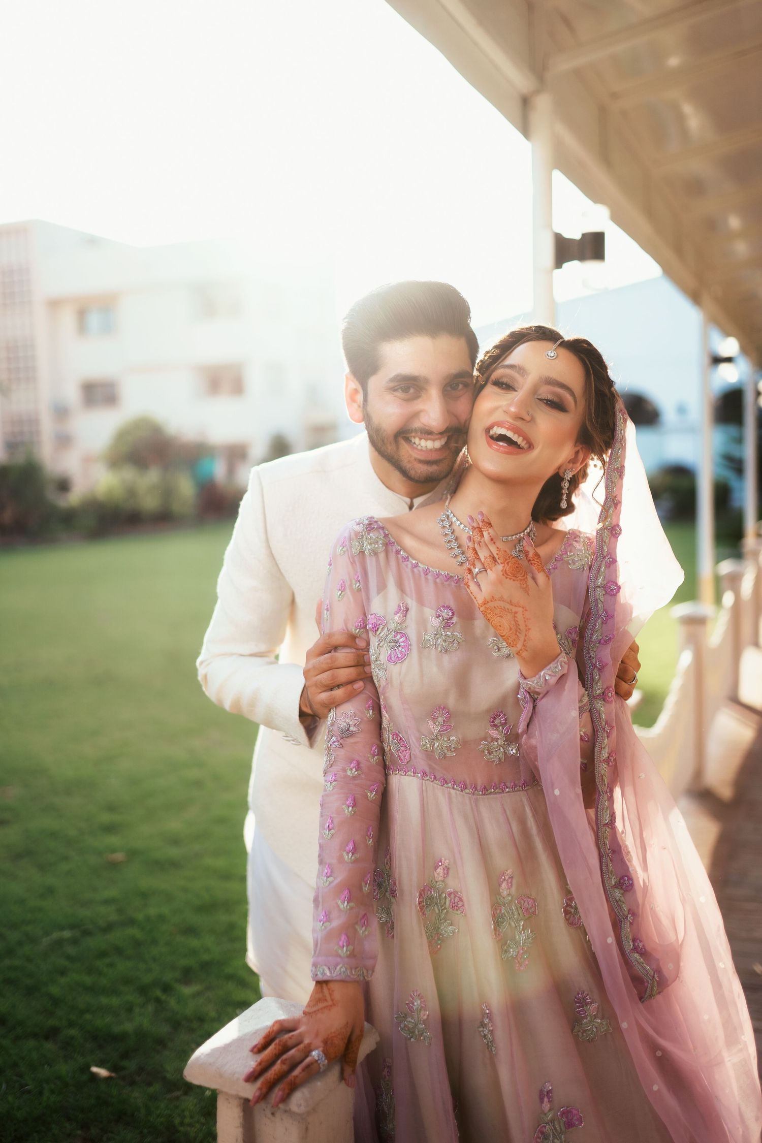 A couple shares lighthearted moments outdoors wearing traditional pink and white South Asian attire.