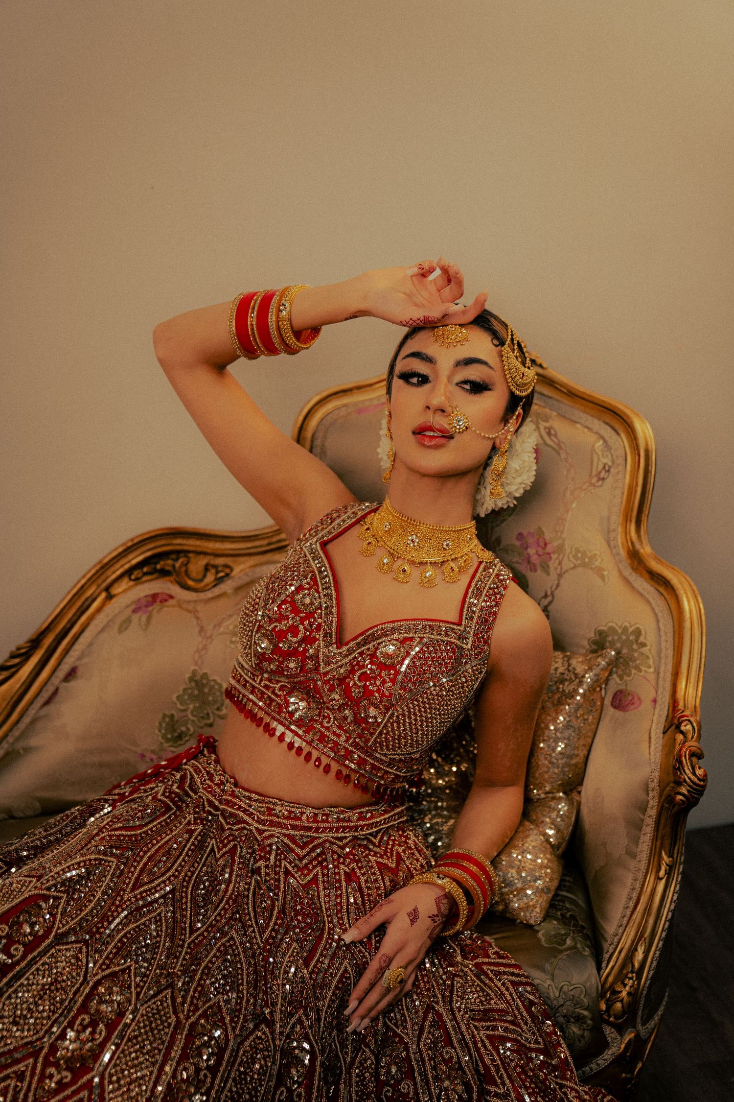 Traditional Indian bridal attire with intricate beadwork and gold jewelry on an antique chaise lounge.