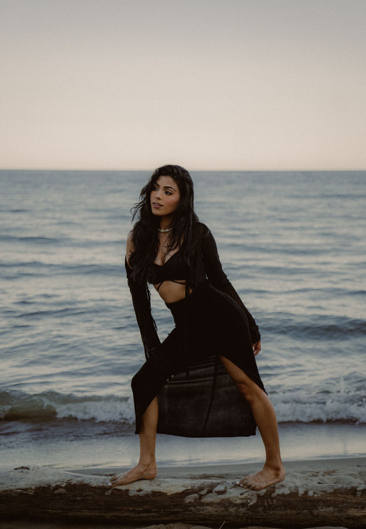 Moody beach photoshoot with waves and dramatic poses in dark clothing.