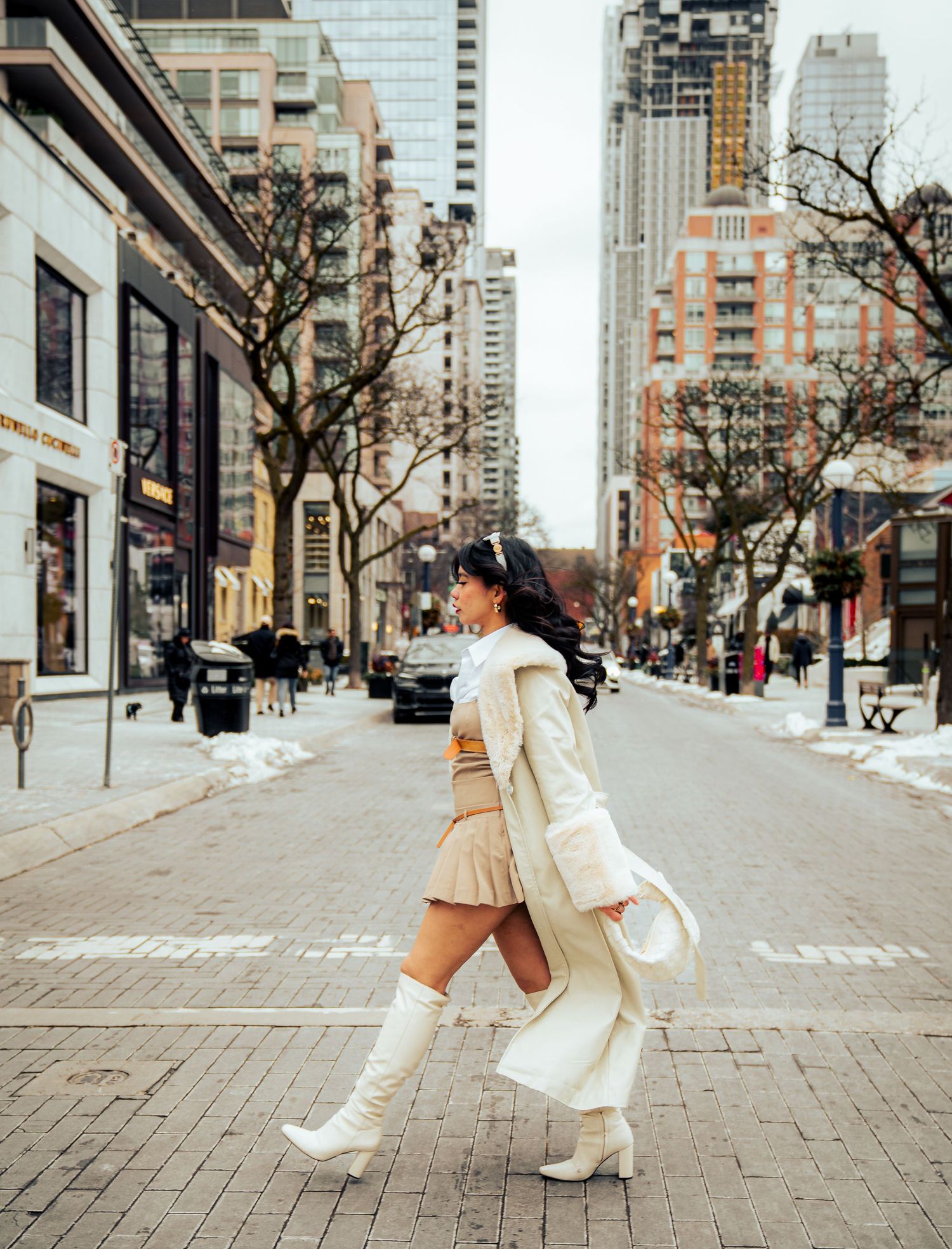 Figure in flowing white outfit dances on urban sidewalk with city buildings in background.