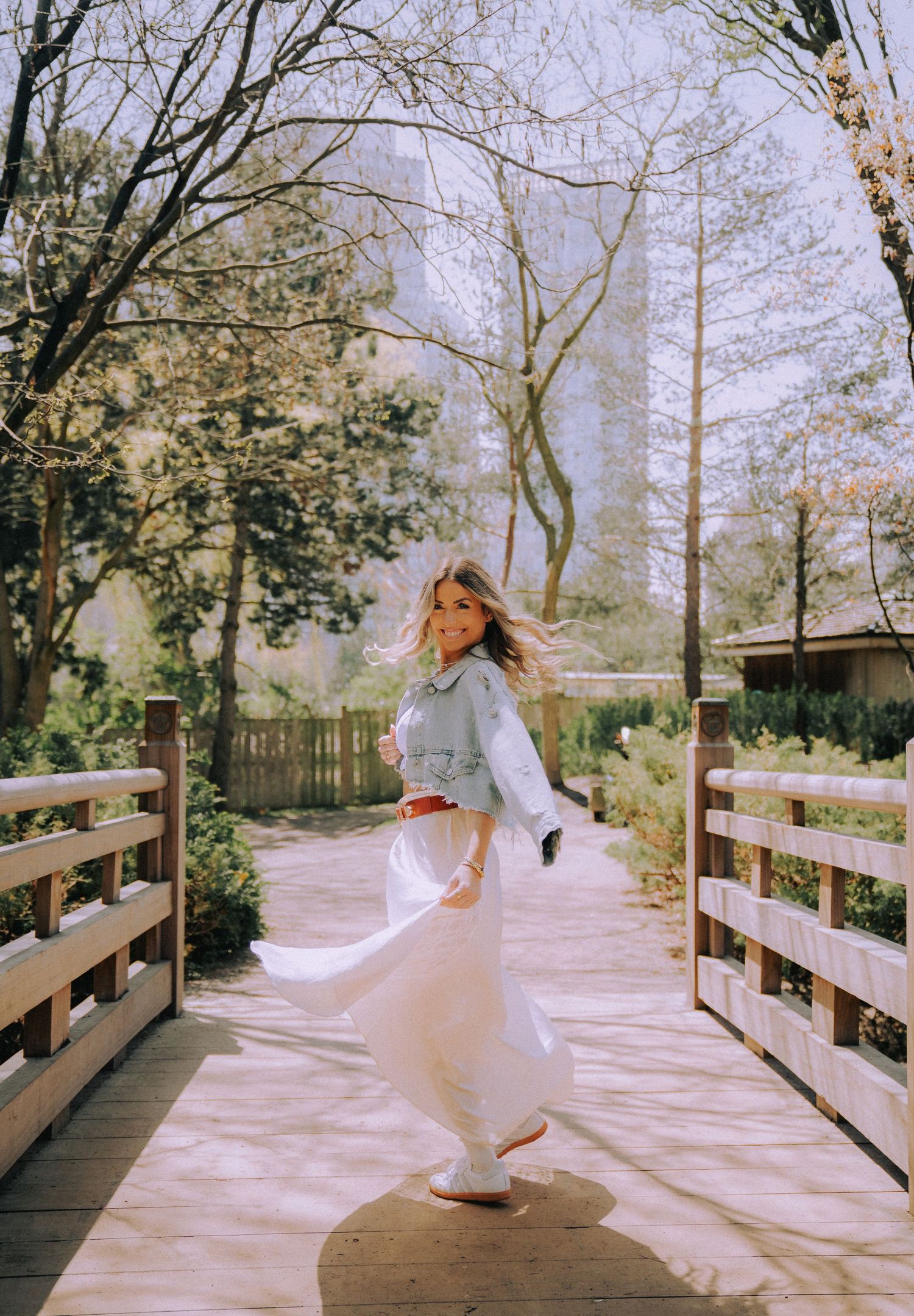 Dreamy portraits in flowing white dress on wooden bridge in nature setting.