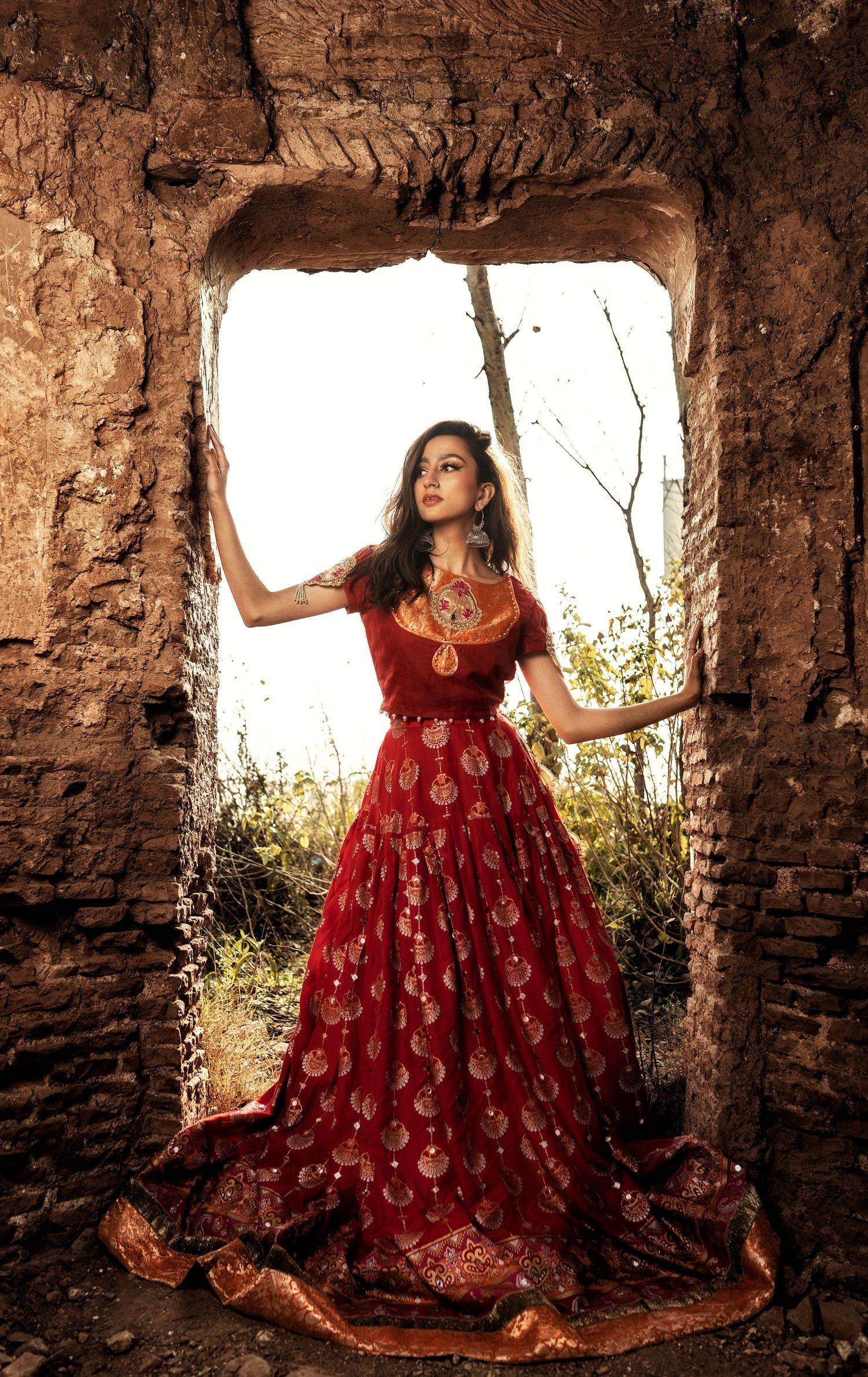 Fashion shoot in stone ruins featuring ornate red and gold traditional dress.