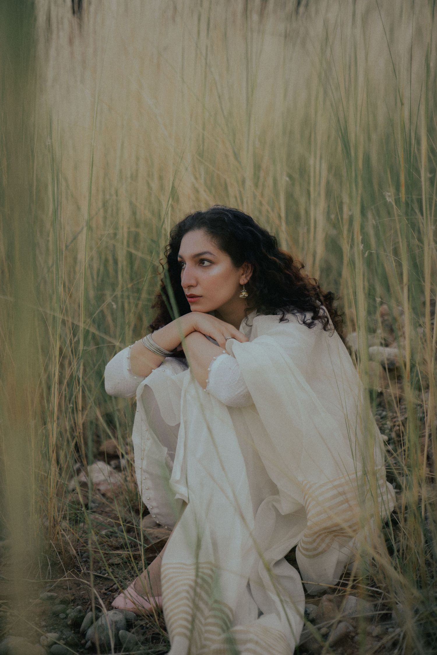Artistic portrait series in tall grass with ethereal white flowing fabric and natural lighting.